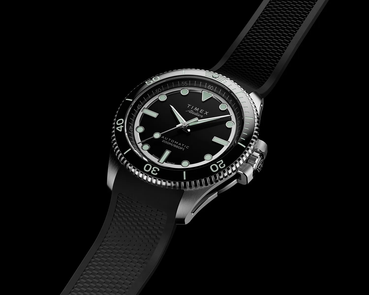 Black Timex wristwatch with a round stainless steel case, luminous hour markers, and hands. The watch face features the text "TIMEX Atelier," "AUTOMATIC," and "200M/660FT." It has a black rotating bezel with minute markings and a textured black rubber strap. The crown is protected by a guard on the right side of the case.
