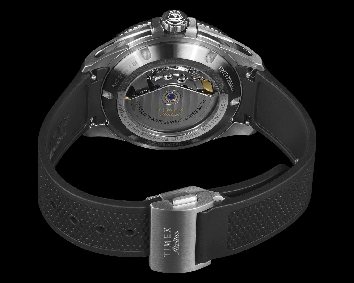 Back view of a Timex Atelier wristwatch featuring a stainless steel case with a transparent sapphire crystal back, showcasing the automatic movement with 29 jewels. The watch has a black textured rubber strap with a stainless steel clasp engraved with "TIMEX Atelier." The crown displays a logo, and the watch is Swiss made.