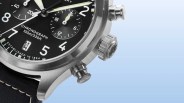 Close-up of a Timex stainless steel chronograph watch with a black dial, white numerals, and luminous hands. The watch face shows subdials, a date window at the 6 o'clock position, and text indicating "CHRONOGRAPH 100m/330ft" and "ESTABLISHED IN 1854." The watch has a black leather strap with white stitching. The crown and pushers are visible on the right side of the case.