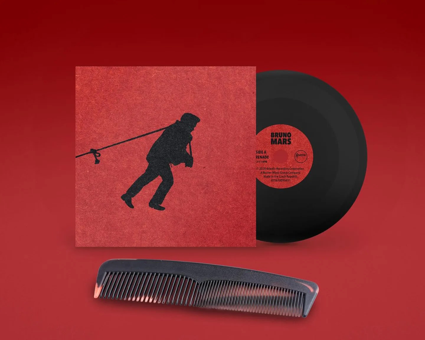 A black vinyl record partially inside a red album cover featuring a silhouette of a man leaning forward with a rope tied around his neck. The record label reads "Bruno Mars" and "Side A Renade 33 1/3 RPM." Below the record and cover is a black comb with fine teeth, all set against a red background.