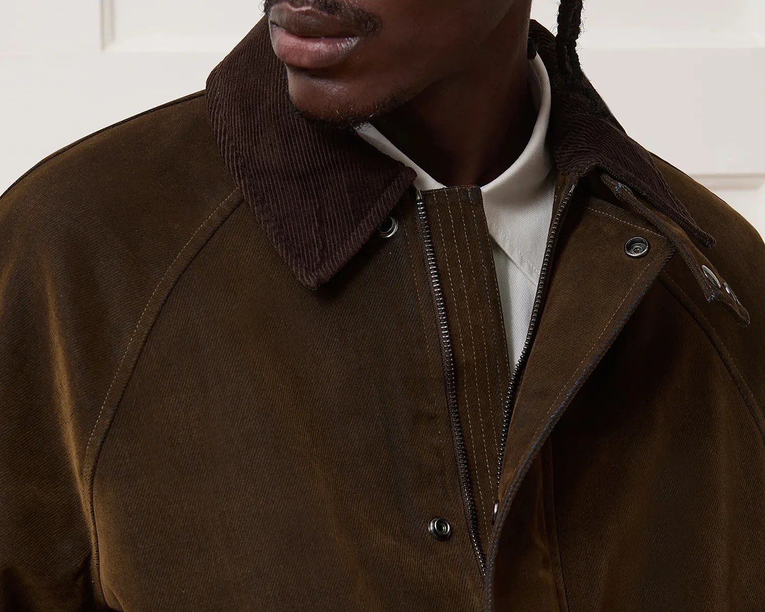 Close-up of a dark brown jacket with a corduroy collar, featuring a zipper and snap button closure, worn over a white shirt.