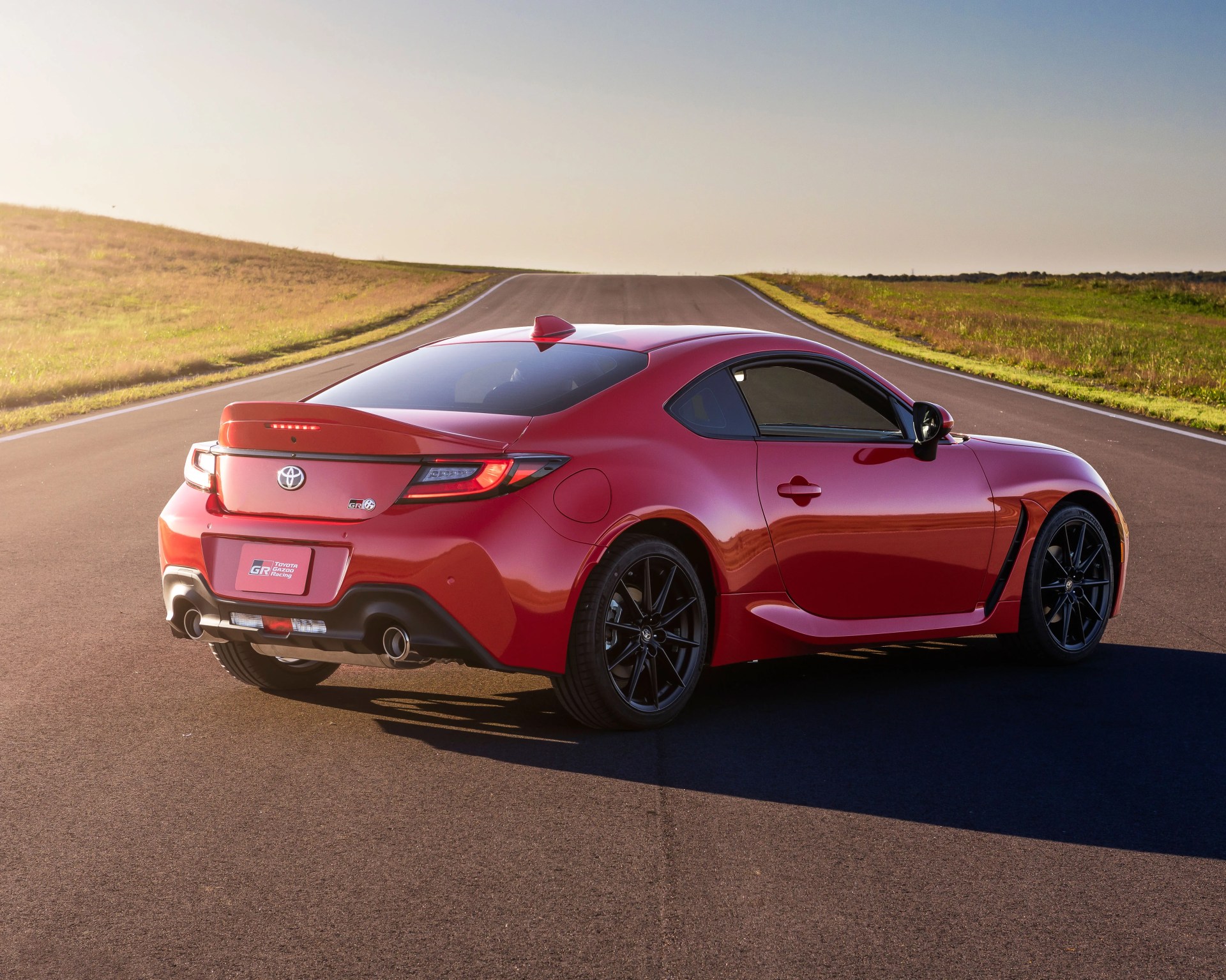 Red Toyota GR sports coupe with black wheels parked on an empty road, viewed from the rear three-quarter angle during daylight.