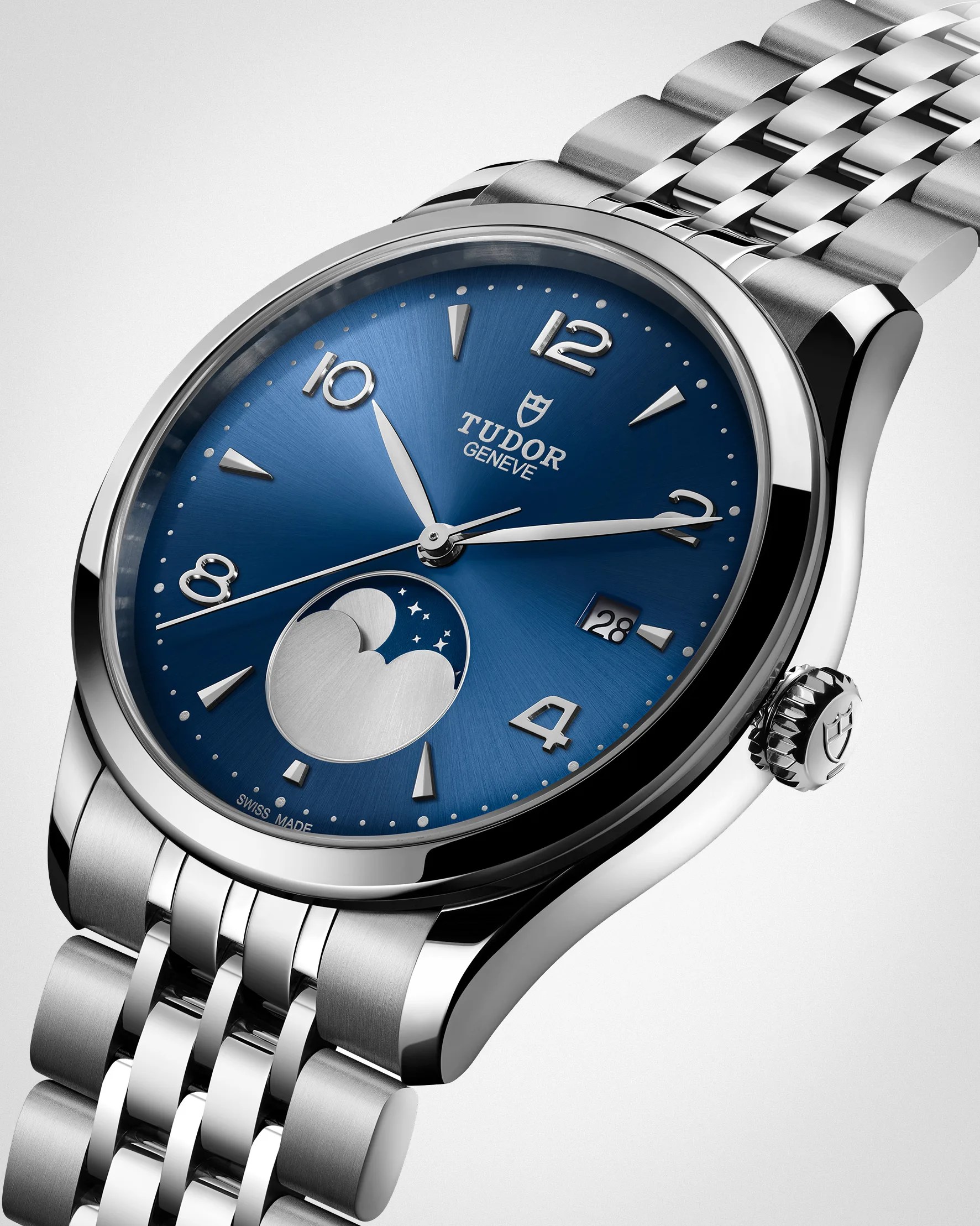 Silver Tudor wristwatch with a blue sunburst dial featuring silver hour markers and hands. The watch includes a moon phase indicator at 6 o'clock, a date window at 3 o'clock, and a polished stainless steel bracelet. The crown is engraved with the Tudor shield logo.