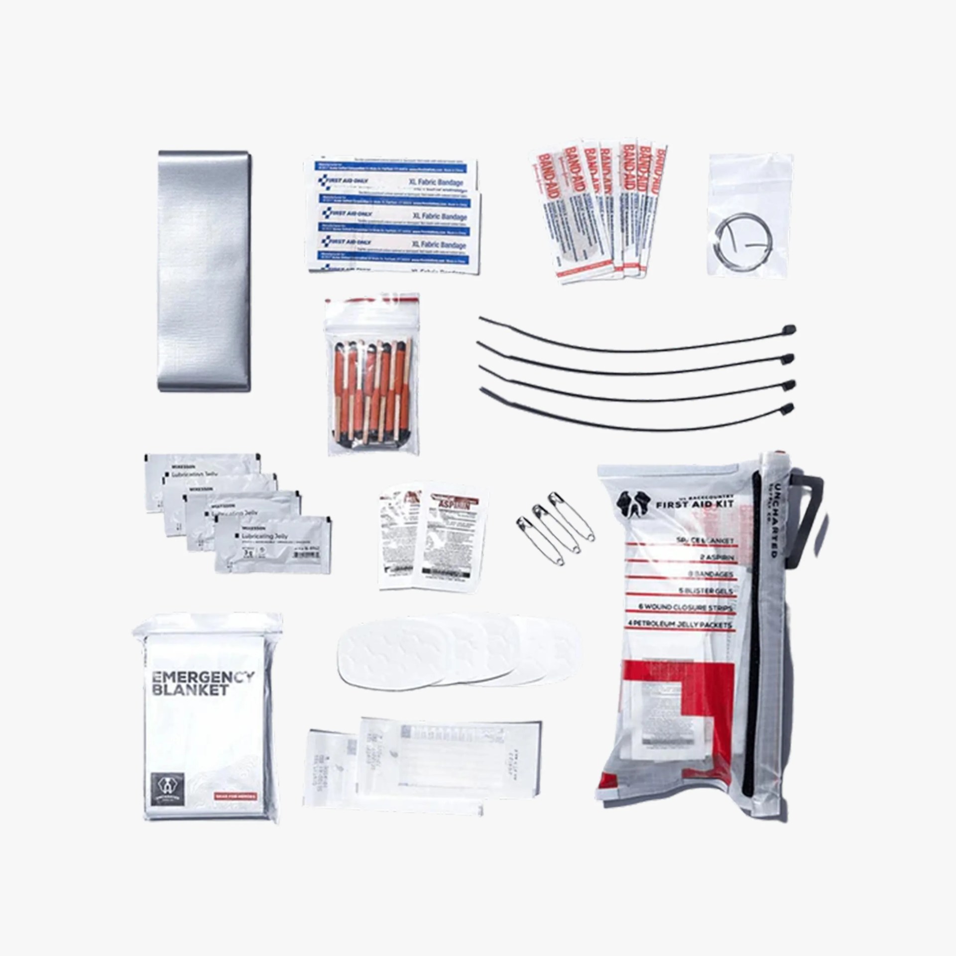 Compact first aid kit with various medical supplies including an emergency blanket, fabric bandages, adhesive bandages, safety pins, wound closure strips, antiseptic wipes, lubricating jelly packets, blister gels, zip ties, and a small pouch containing additional items. The kit is organized neatly on a white background.