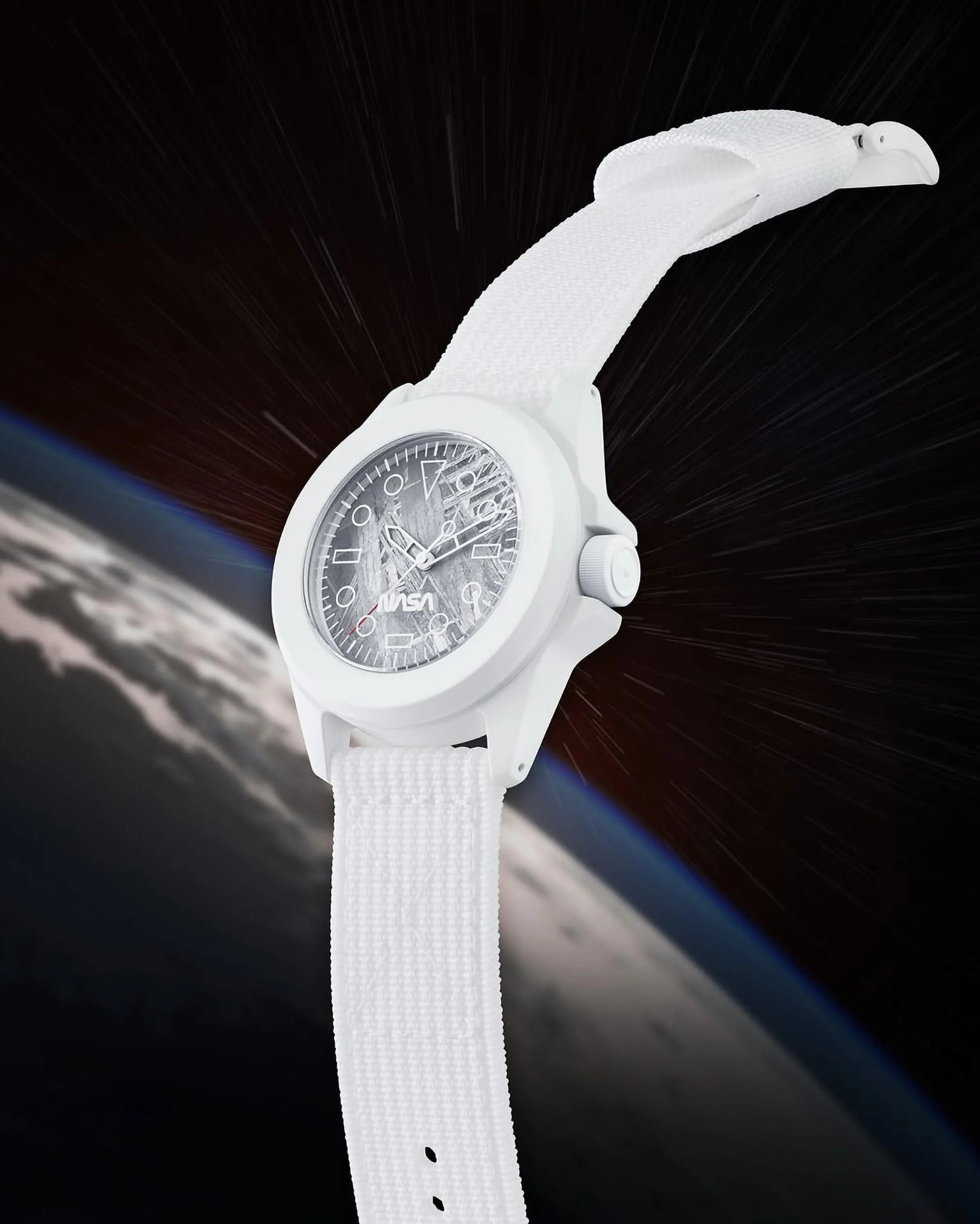 White wristwatch with a textured fabric strap and a round face featuring the NASA logo. The watch face has a scratched or distressed design with white hour markers and hands. The background shows a view of Earth from space with a dark starry sky.