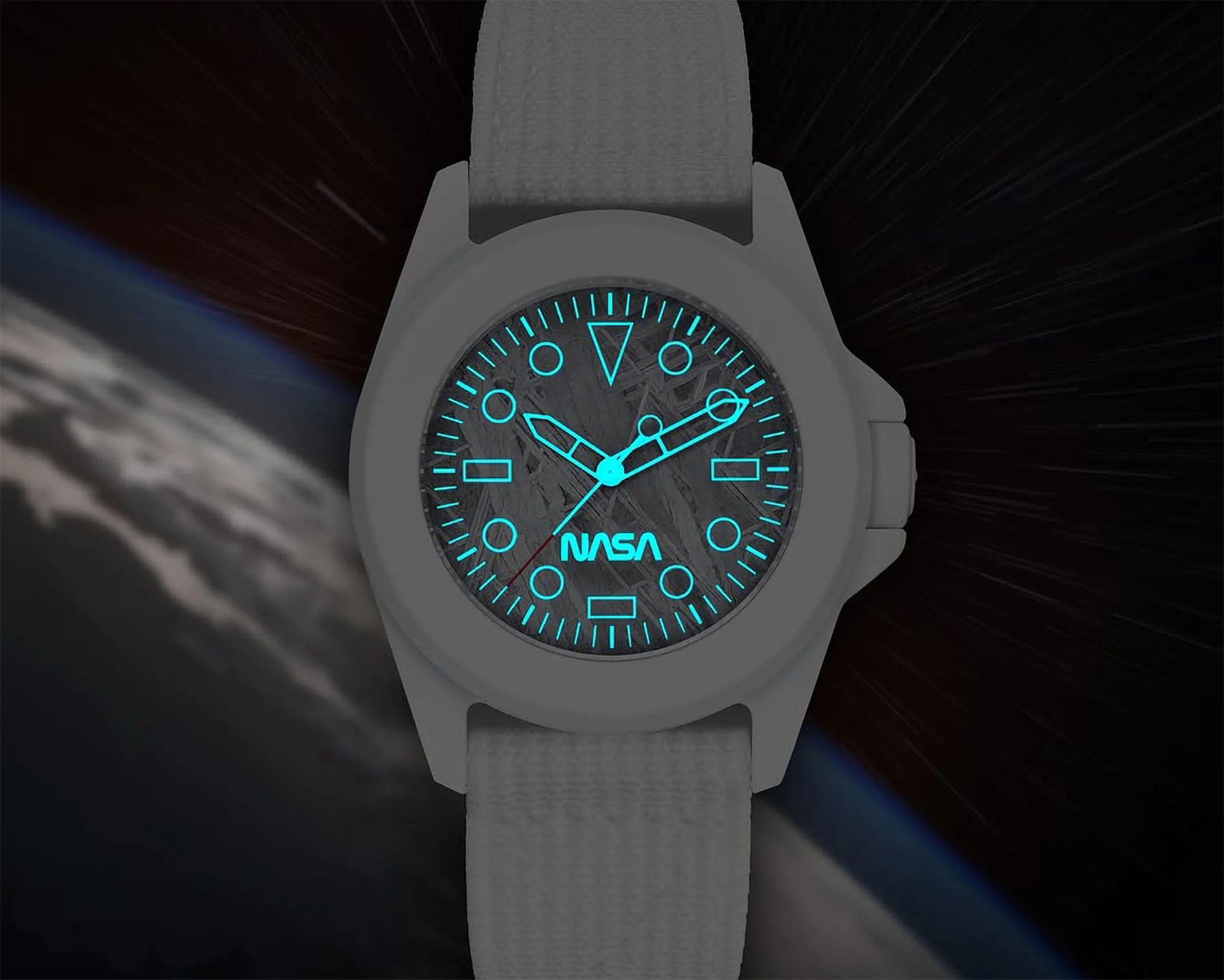 A gray wristwatch with a textured strap and a round face displaying glowing blue hour markers and hands. The watch face features the NASA logo and has a dark, textured background. The watch is set against a space-themed backdrop showing part of Earth and a starry sky.