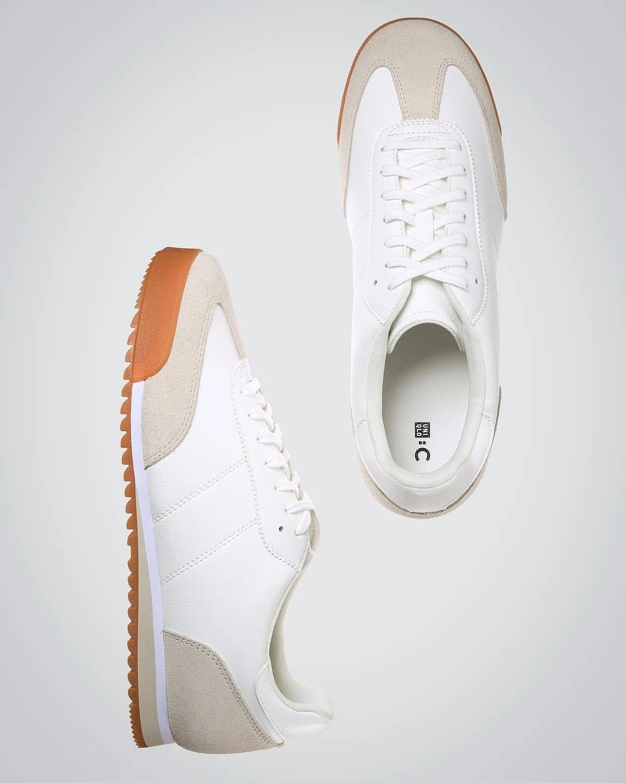 Pair of white sneakers with beige suede accents on the toe and heel, white laces, and a brown rubber sole with a ridged pattern. One shoe is shown from the side and the other from the top.