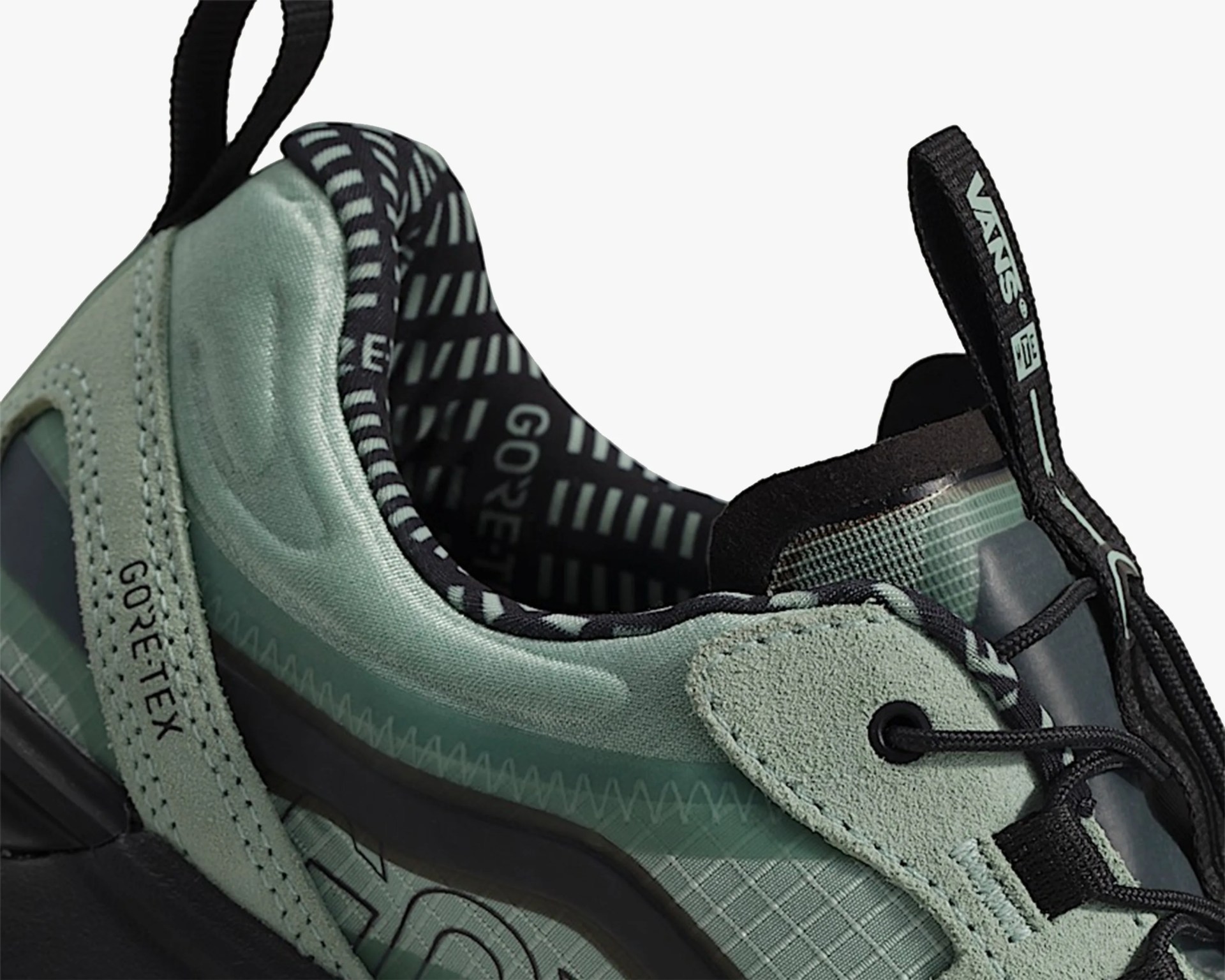 Close-up of a green and black sneaker featuring Gore-Tex material. The shoe has a textured fabric upper with suede overlays, black laces, and a pull tab on the tongue with the Vans and DC logos. The interior lining is black with light green patterns and the word "GORE" visible. The midsole is black with a translucent section.