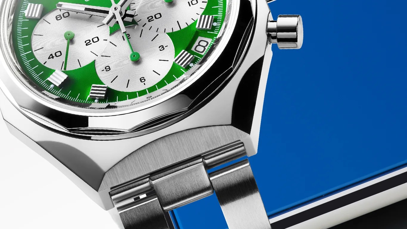 Close-up of a silver wristwatch with a green dial featuring three silver subdials, silver hands, and striped rectangular hour markers. The watch has a stainless steel case and bracelet, with a polished bezel and a crown on the right side. The background is blue.