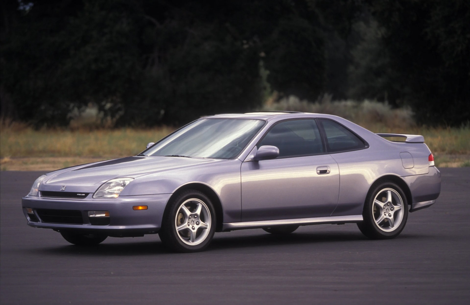 Silver two-door Honda Prelude coupe parked on asphalt with trees in the background.