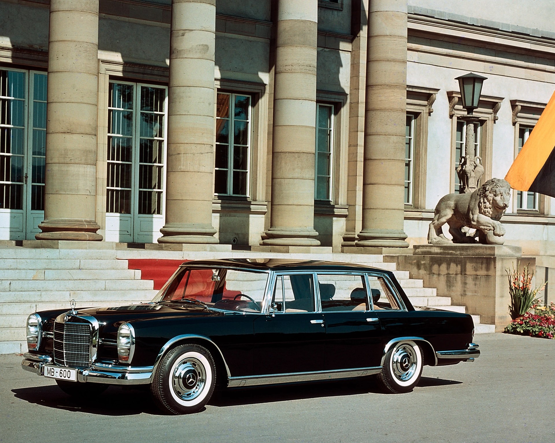 Black vintage Mercedes-Benz 600 sedan parked in front of a building with large stone columns and a lion statue.