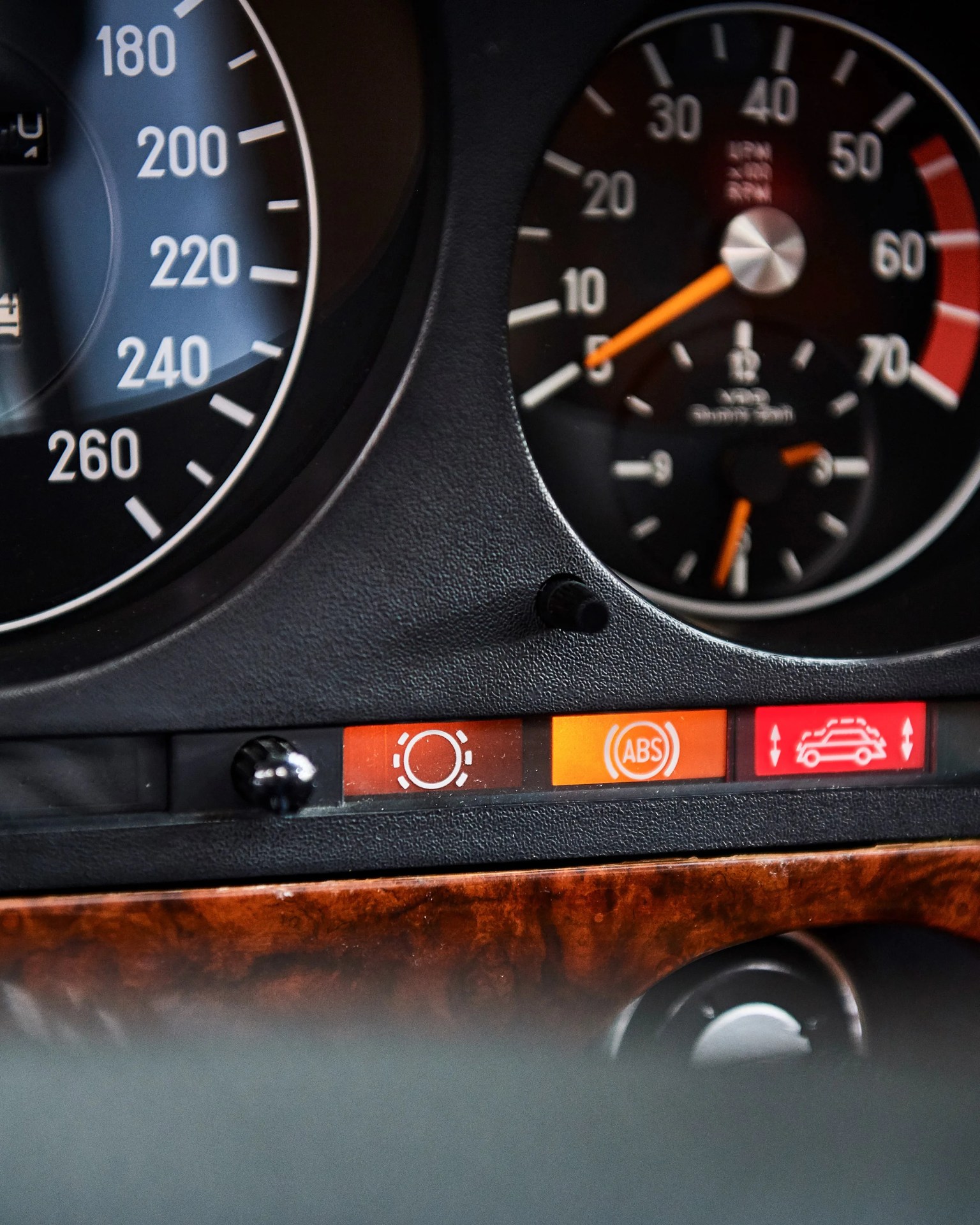 Close-up of a car dashboard showing illuminated warning lights for brake system, ABS, and suspension with speedometer and tachometer dials.