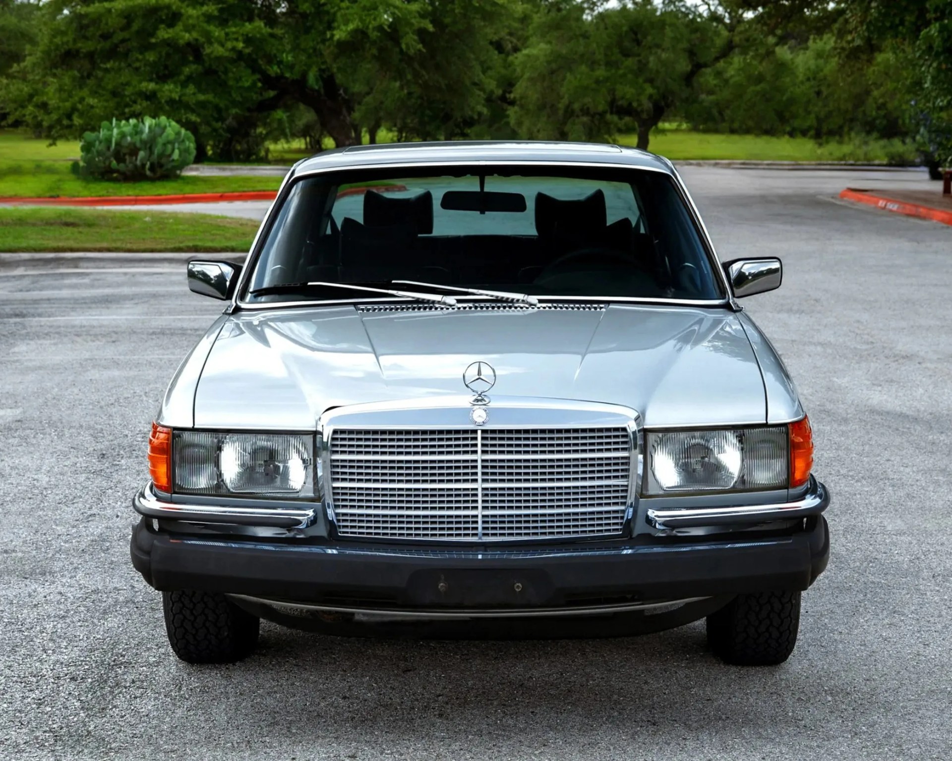 Silver classic Mercedes-Benz sedan with large front grille and orange turn signals parked on a paved road.