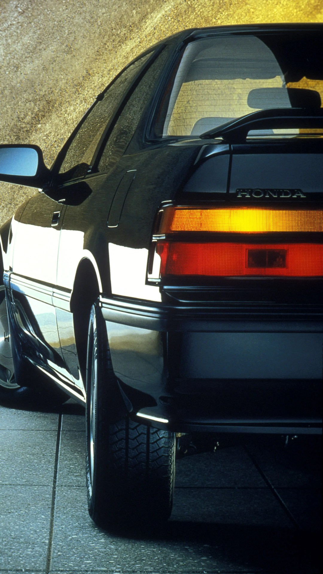 Rear side view of a black Honda car showing the taillight and rear tire on a tiled floor.