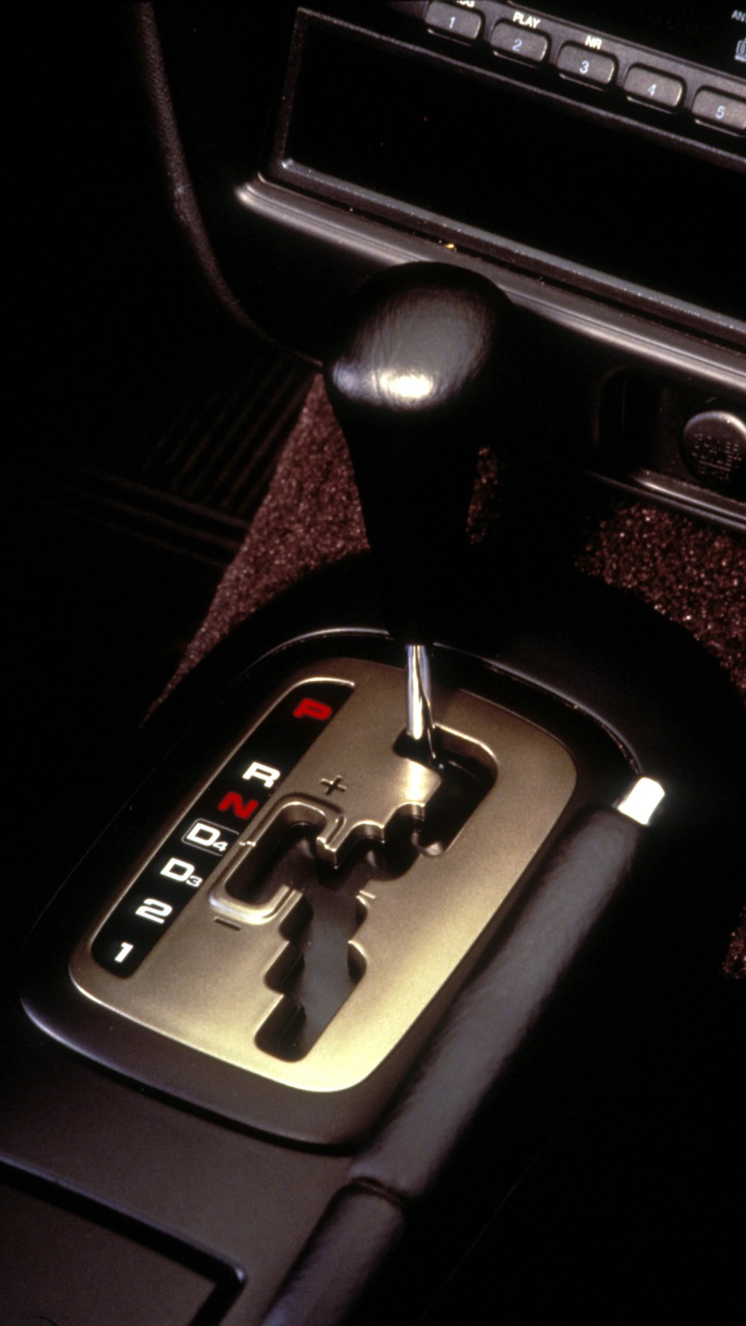 Automatic gear shift lever with black leather knob and illuminated gear indicators in a car center console.