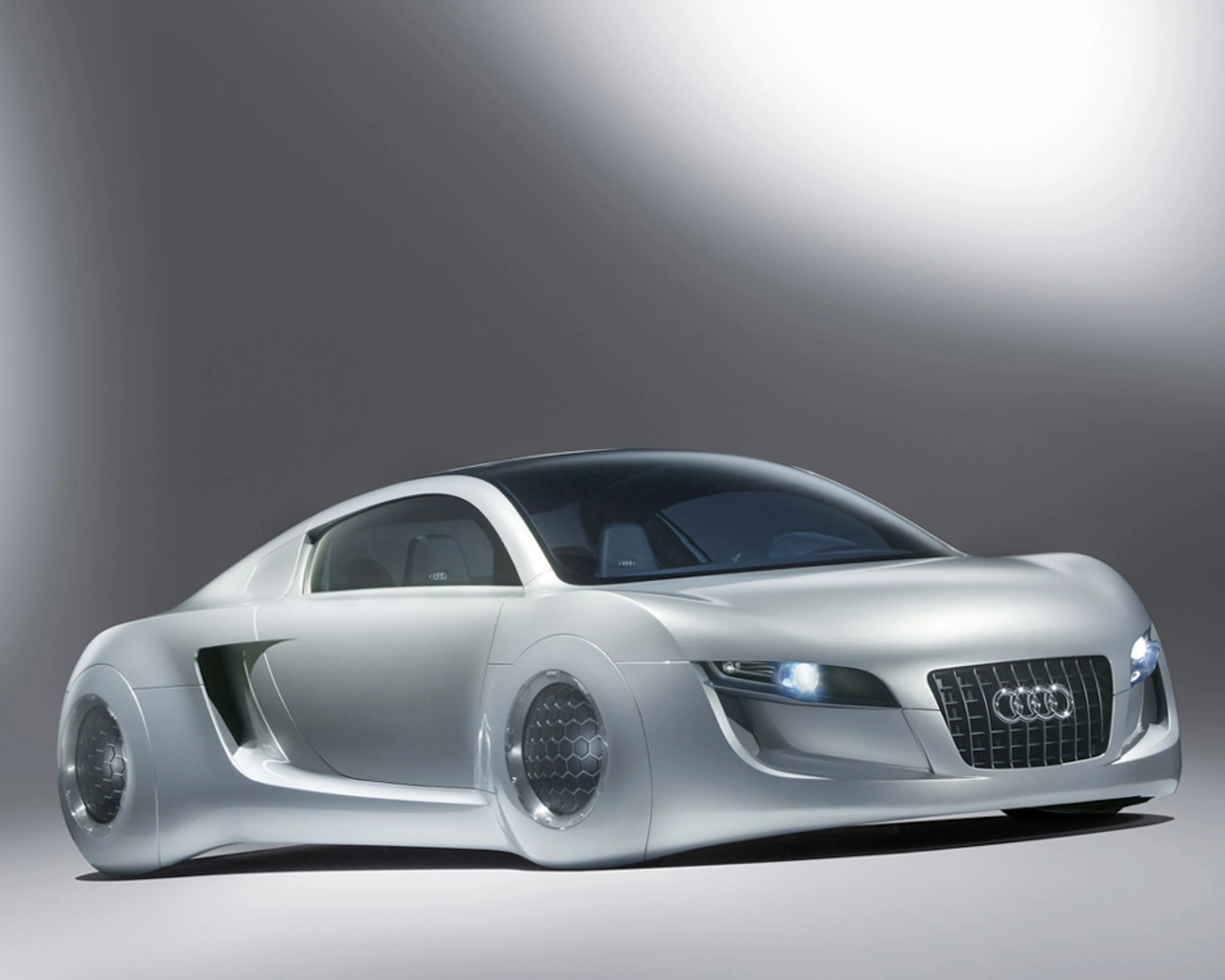 Silver futuristic Audi sports car with smooth, rounded body and honeycomb-patterned wheels on a gray background.
