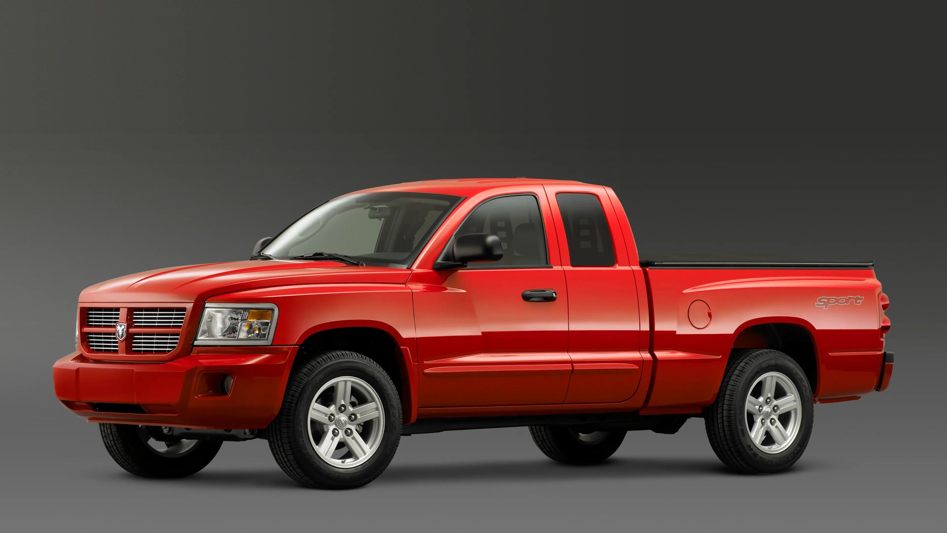 Red Dodge Dakota Sport pickup truck with extended cab and silver alloy wheels on gray background.