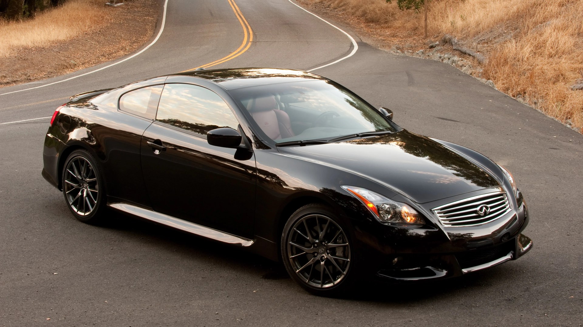 Black Infiniti coupe with tinted windows and sporty black alloy wheels parked on a winding road.
