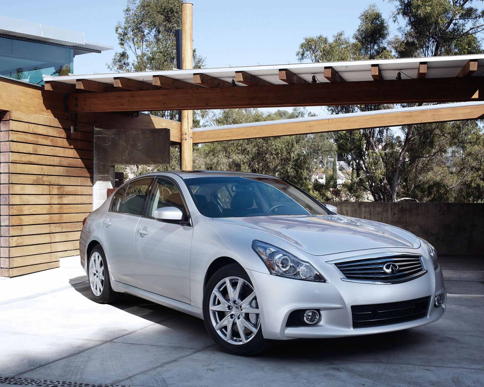 Silver Infiniti sedan parked under a wooden pergola with trees in the background.