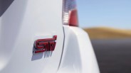 Red and black STI badge on the rear white panel of a car with a blurred taillight and road background.