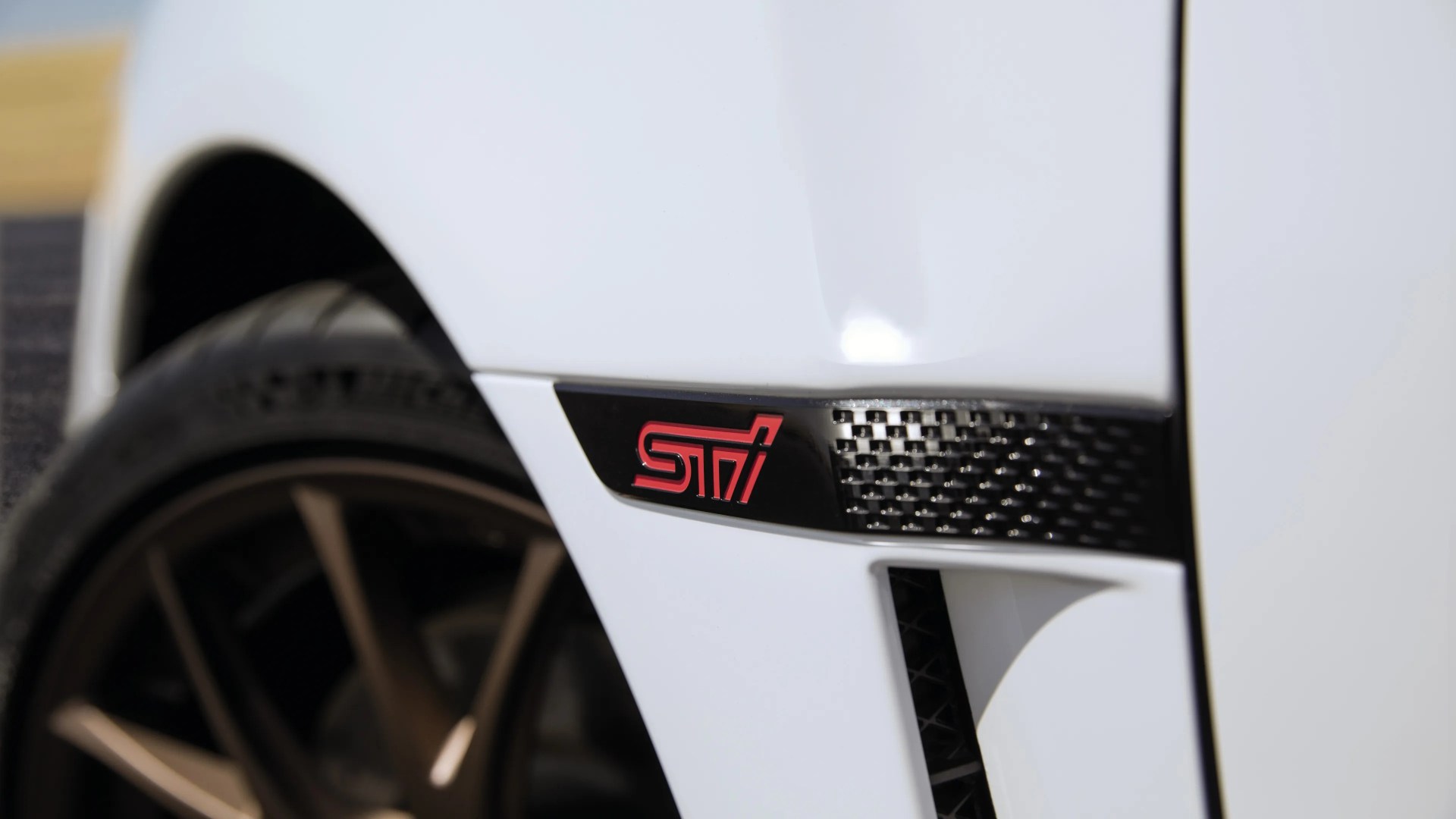 Close-up of a white car fender with a black and red STI badge and bronze wheel in the background.
