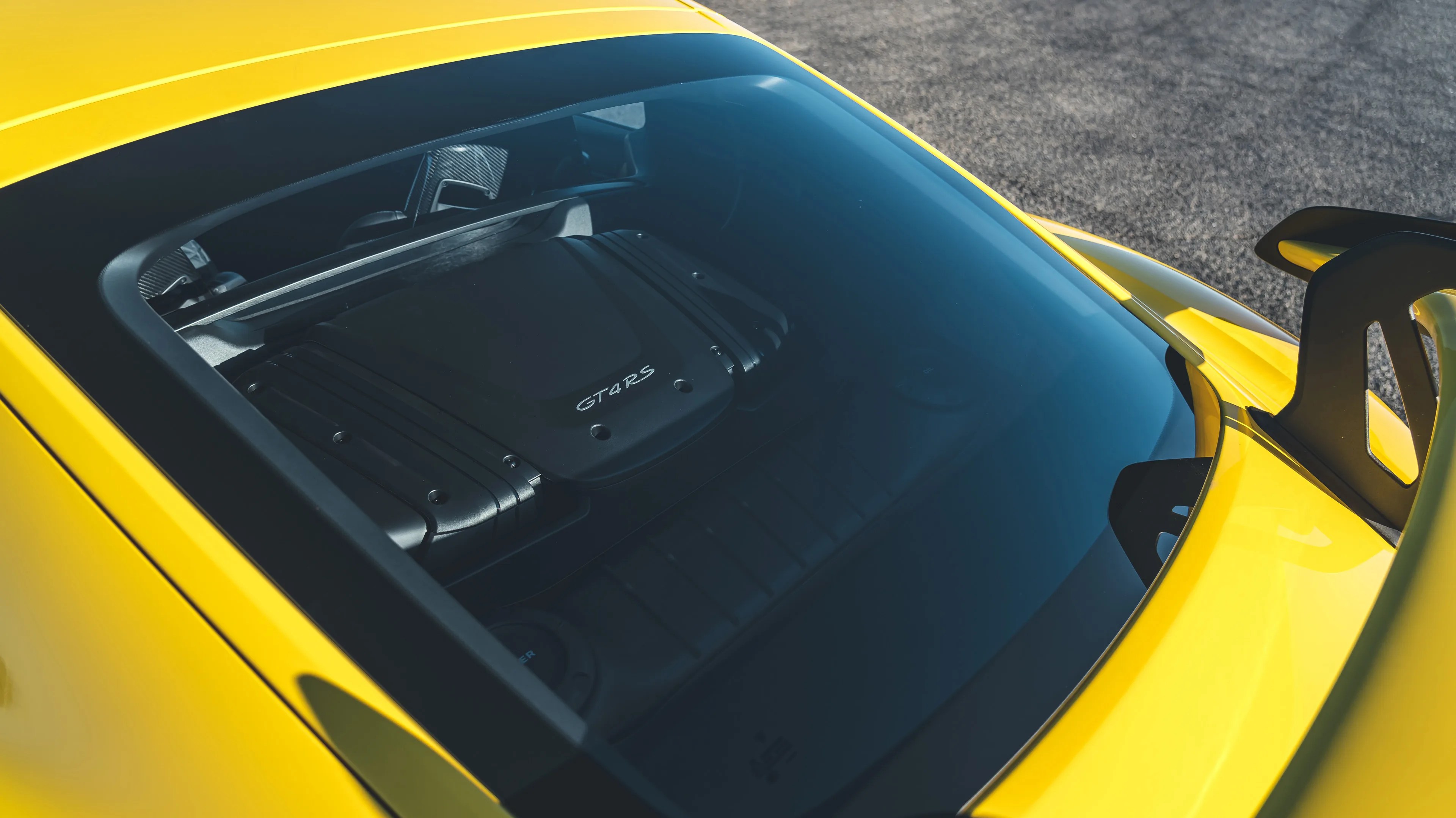 Yellow sports car rear window showing a black engine cover labeled "GT4 RS" and a rear spoiler.
