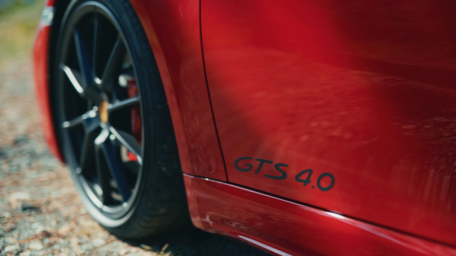 Close-up of a red car's side panel with "GTS 4.0" badge and black alloy wheel on gravel.