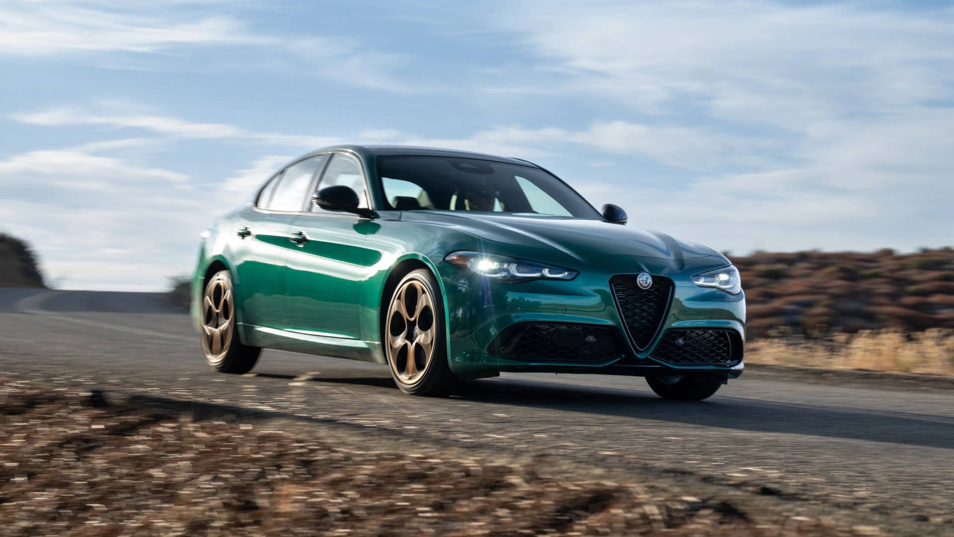 Green Alfa Romeo sedan with bronze five-hole wheels driving on a paved road.