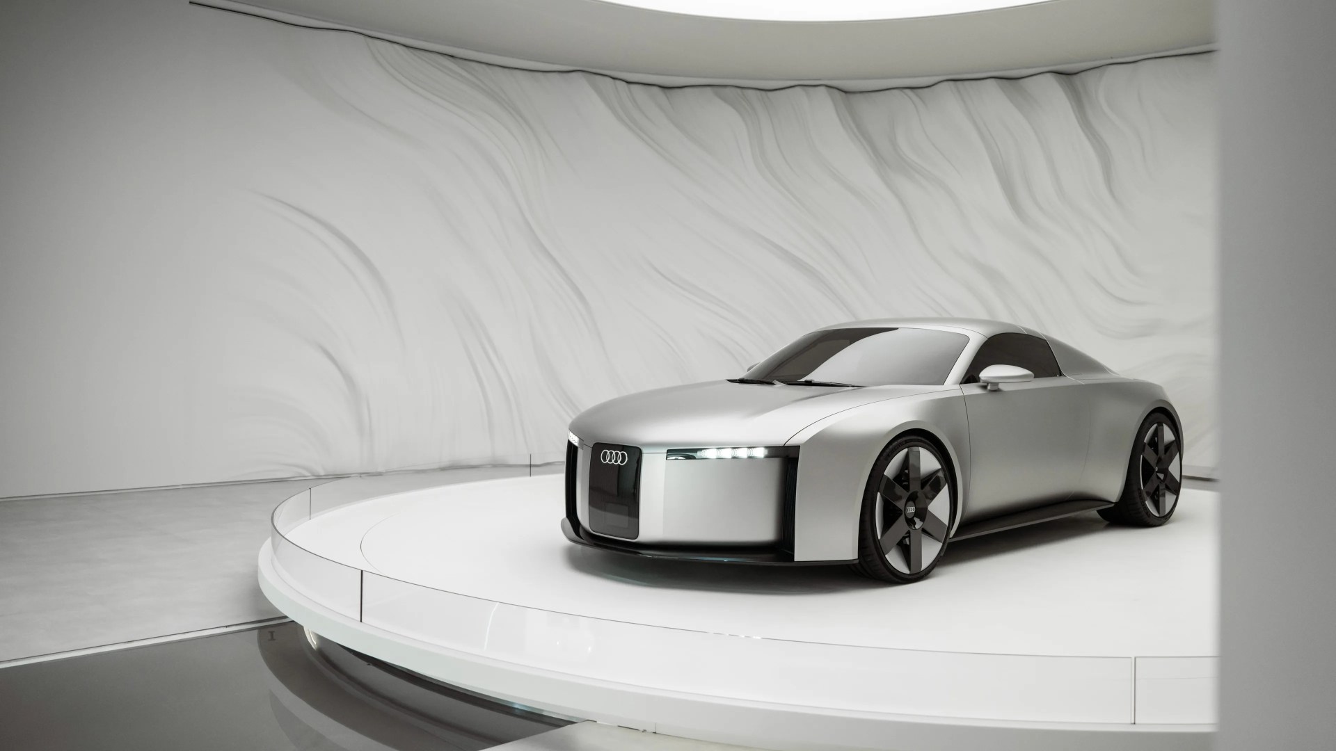 Silver Audi concept car with black tinted windows on a white circular platform in a modern showroom.