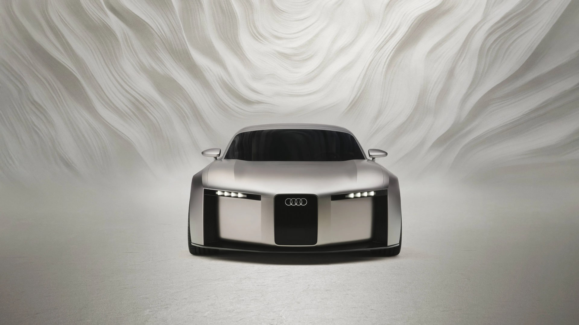 Silver Audi concept car with sleek, futuristic design and illuminated headlights against a textured white background.