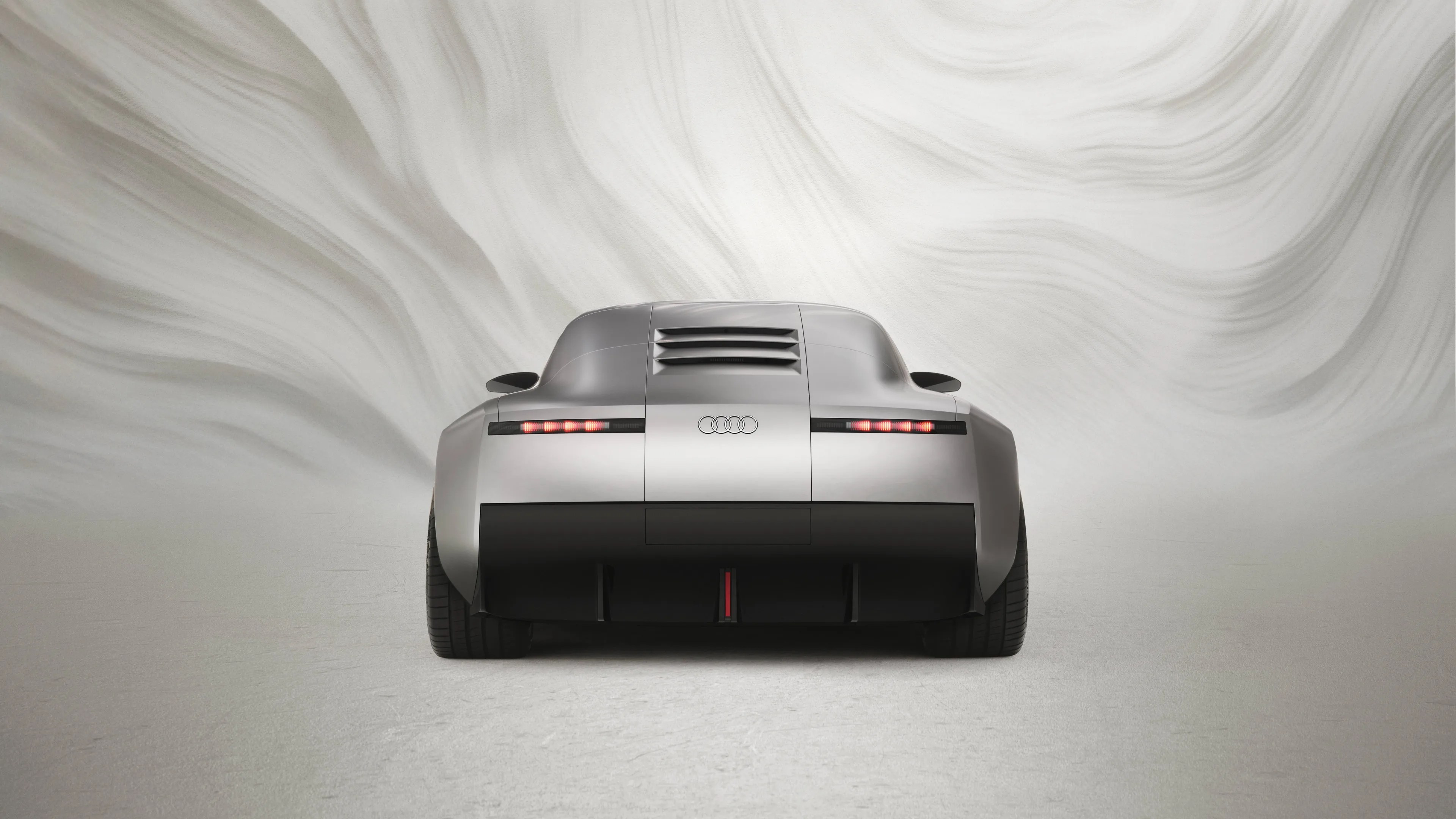 Rear view of a silver Audi sports car with horizontal taillights and black lower bumper against a marbled gray background.