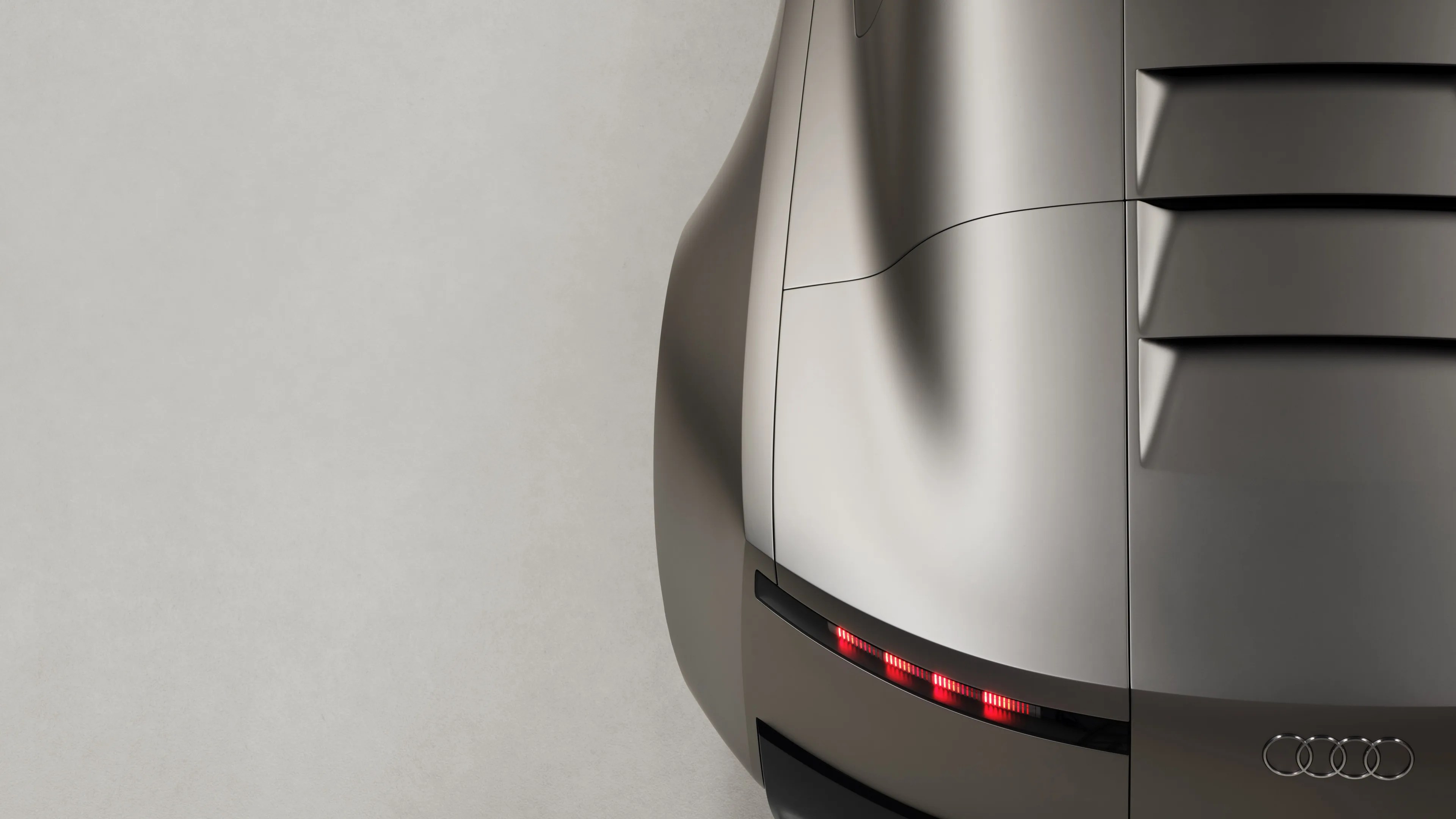 Rear corner of a silver Audi car showing taillights and the Audi logo on a light background.