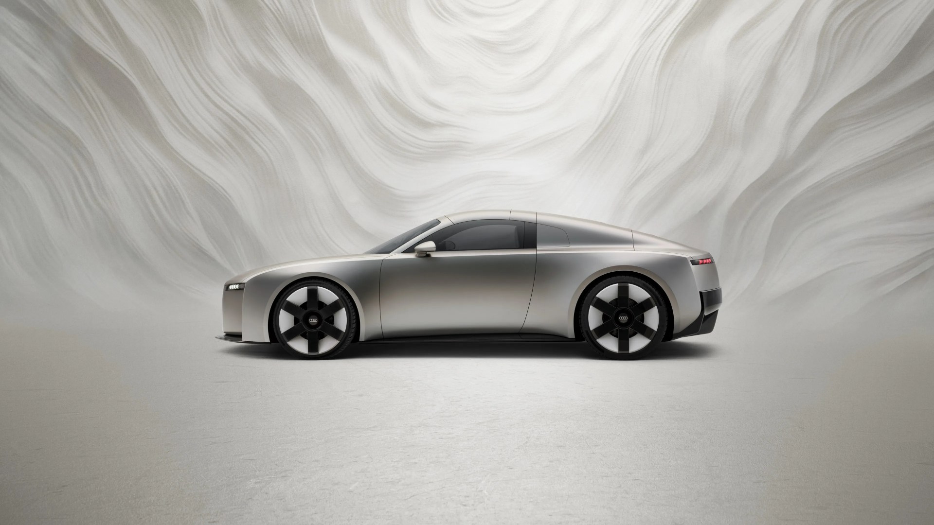Silver sleek Audi electric sports car with black five-spoke wheels on a light textured floor.