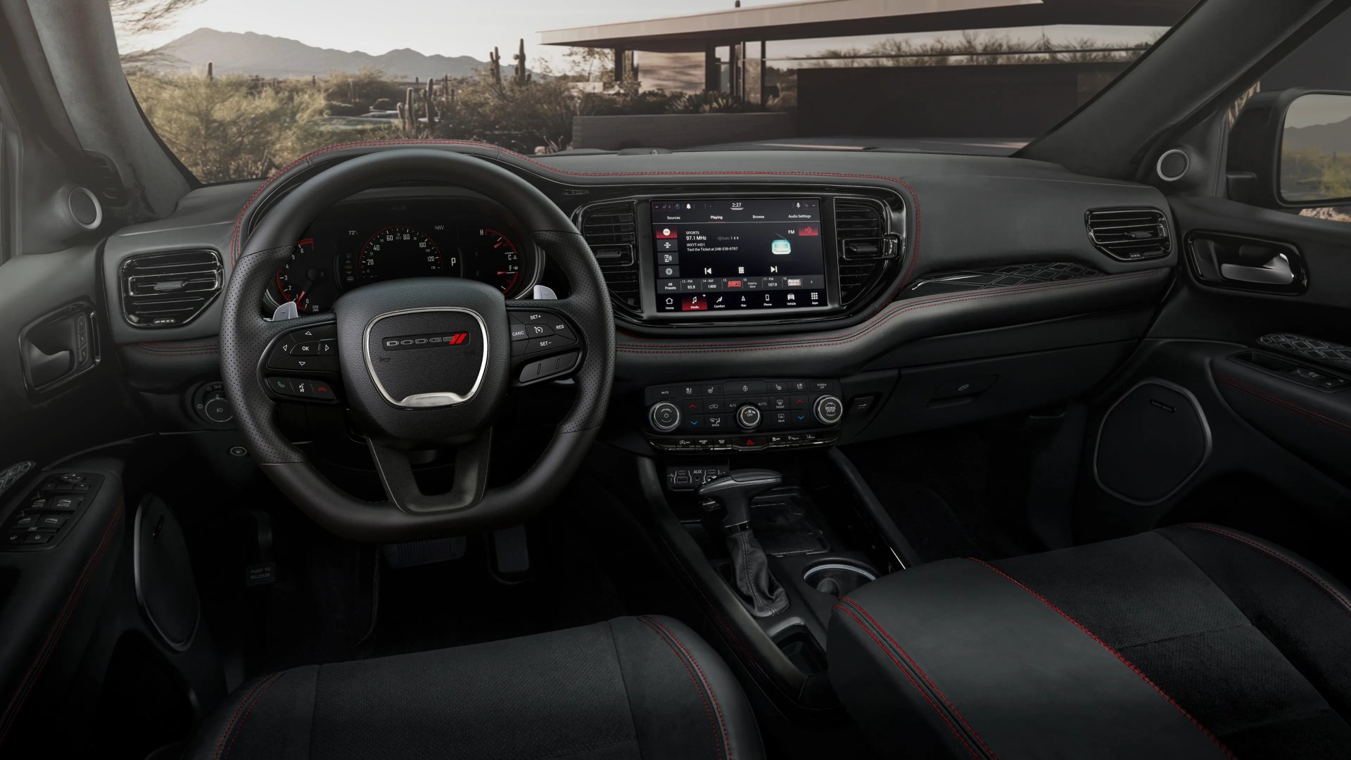 Black Dodge steering wheel with red stitching and central logo, digital dashboard, and touchscreen infotainment system in a black interior.