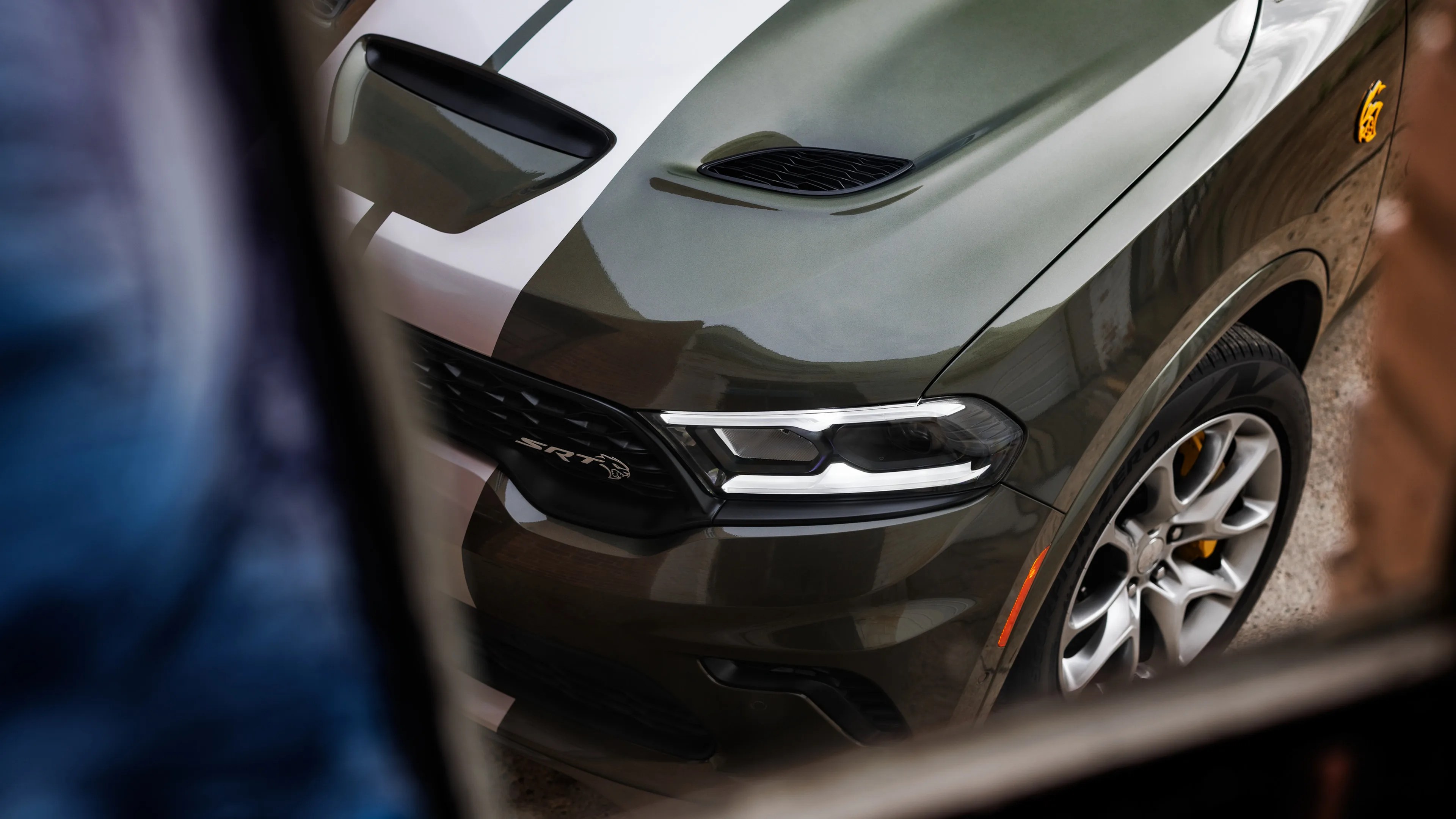 Front view of a dark green Dodge Durango SRT with white racing stripes and yellow brake calipers.