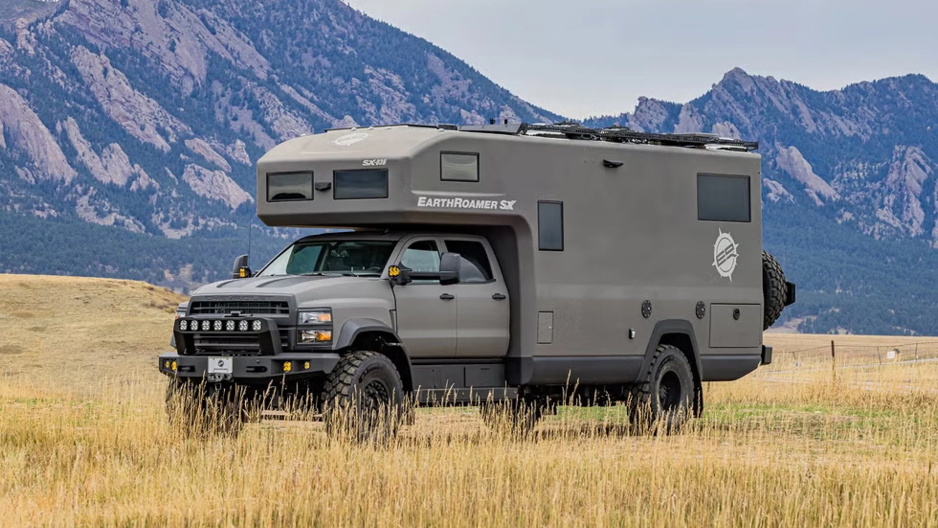 Gray EarthRoamer SX off-road camper truck parked in a grassy field with mountains in the background.