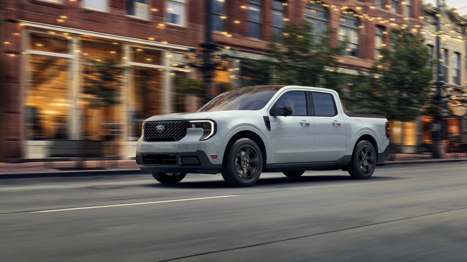 Light gray Ford electric pickup truck driving on a city street with blurred buildings in the background.