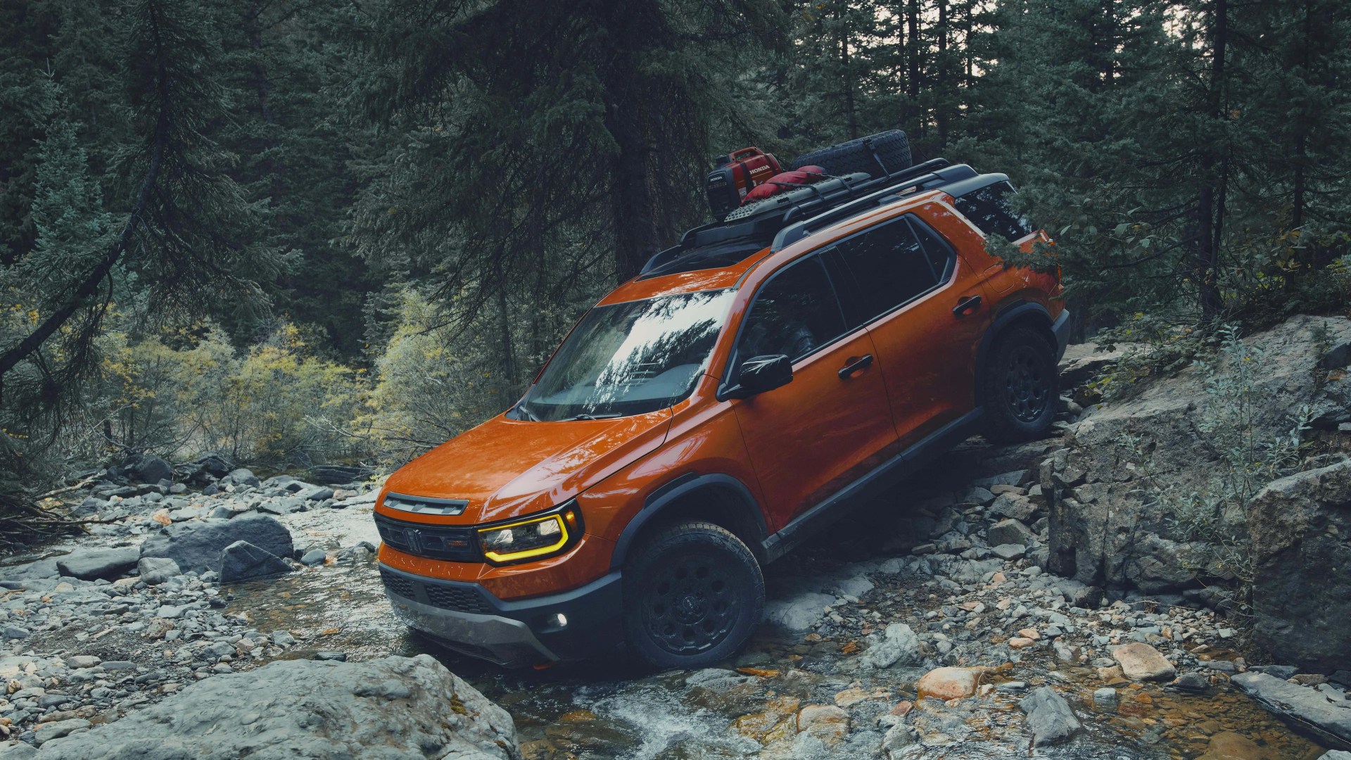Orange off-road SUV with roof rack and spare tire driving on rocky stream in forest.
