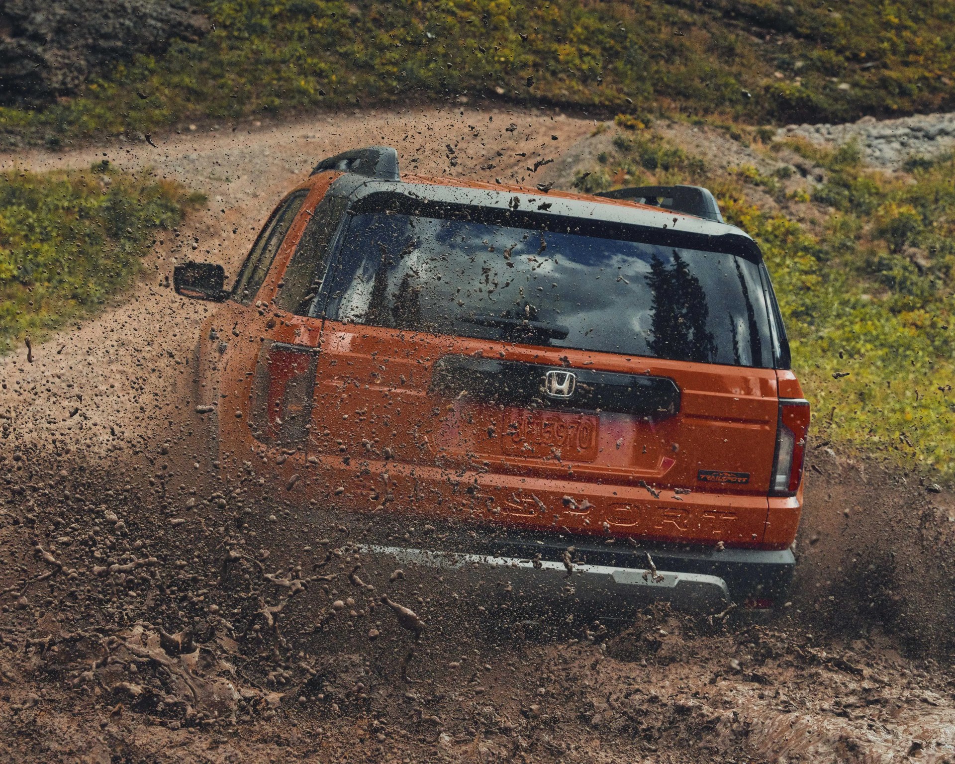 Orange Honda SUV driving on a muddy dirt road with mud splashing behind it.