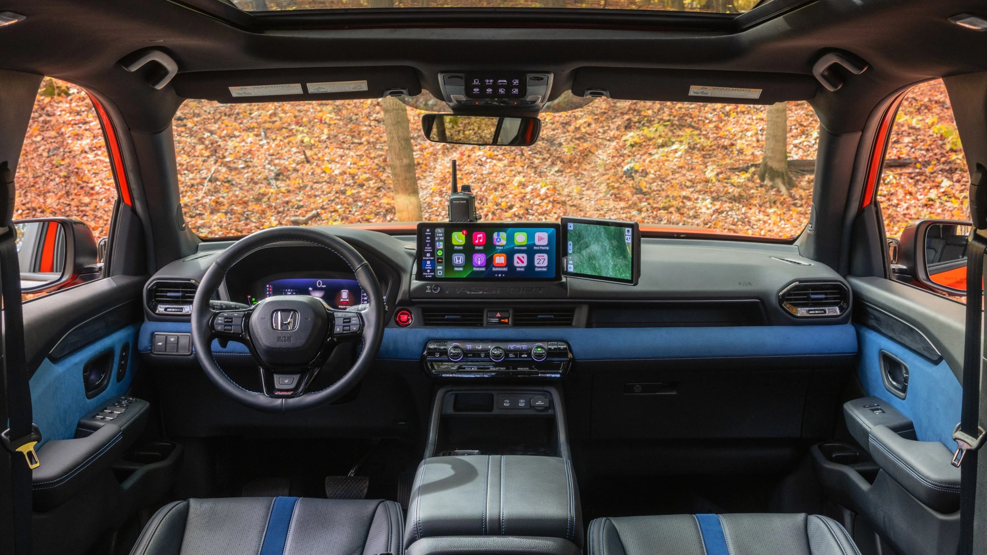 Car interior with black and blue leather seats, digital dashboard, dual touchscreen displays, and panoramic sunroof.
