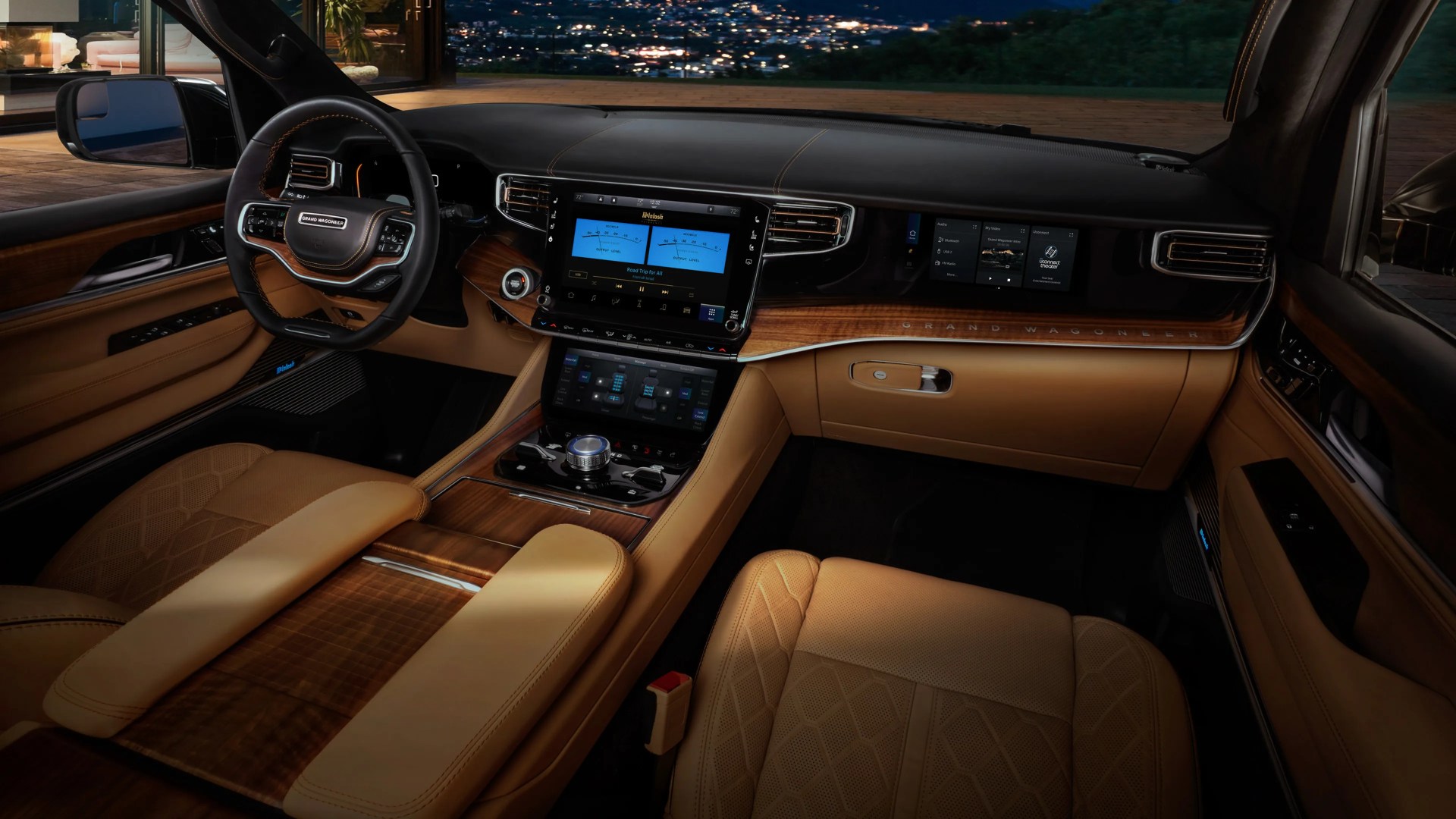 Luxury car interior with tan leather seats, wood trim, dual touchscreen displays, and a black leather steering wheel.