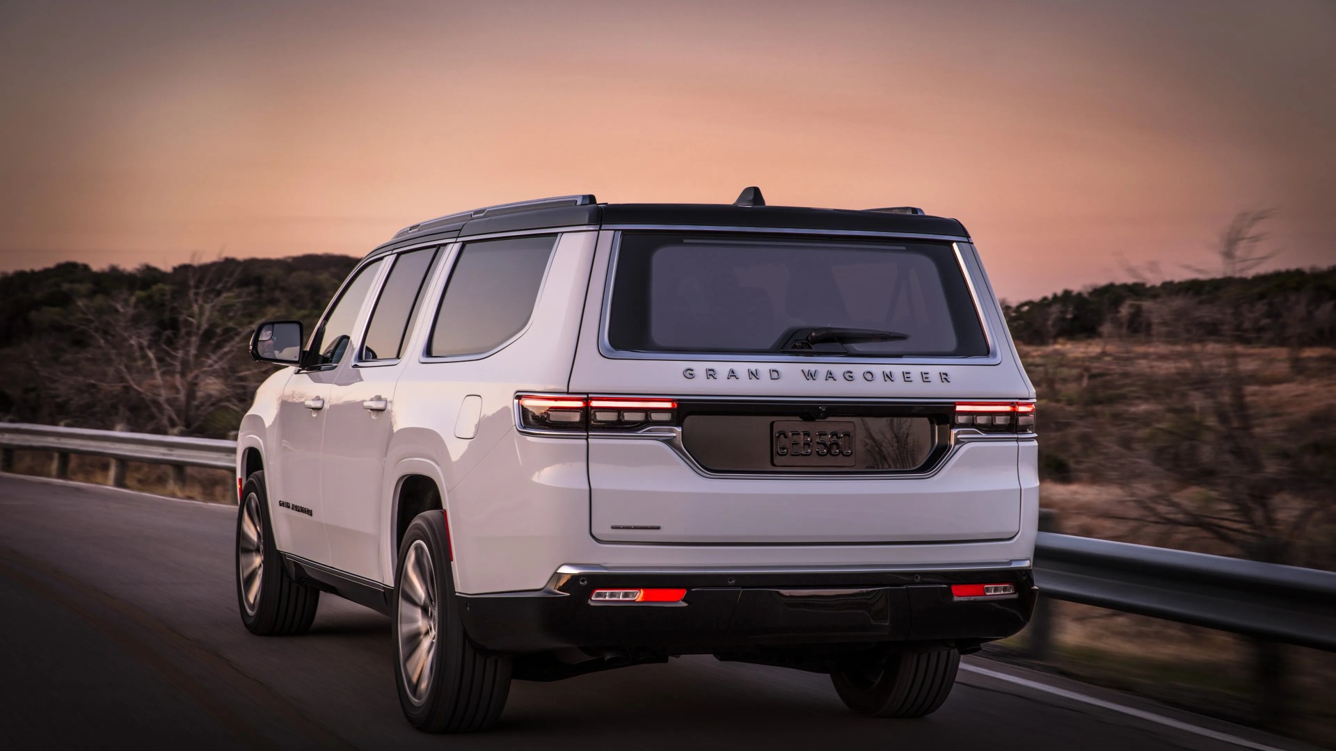 White Grand Wagoneer SUV driving on a road at sunset with rear lights illuminated.