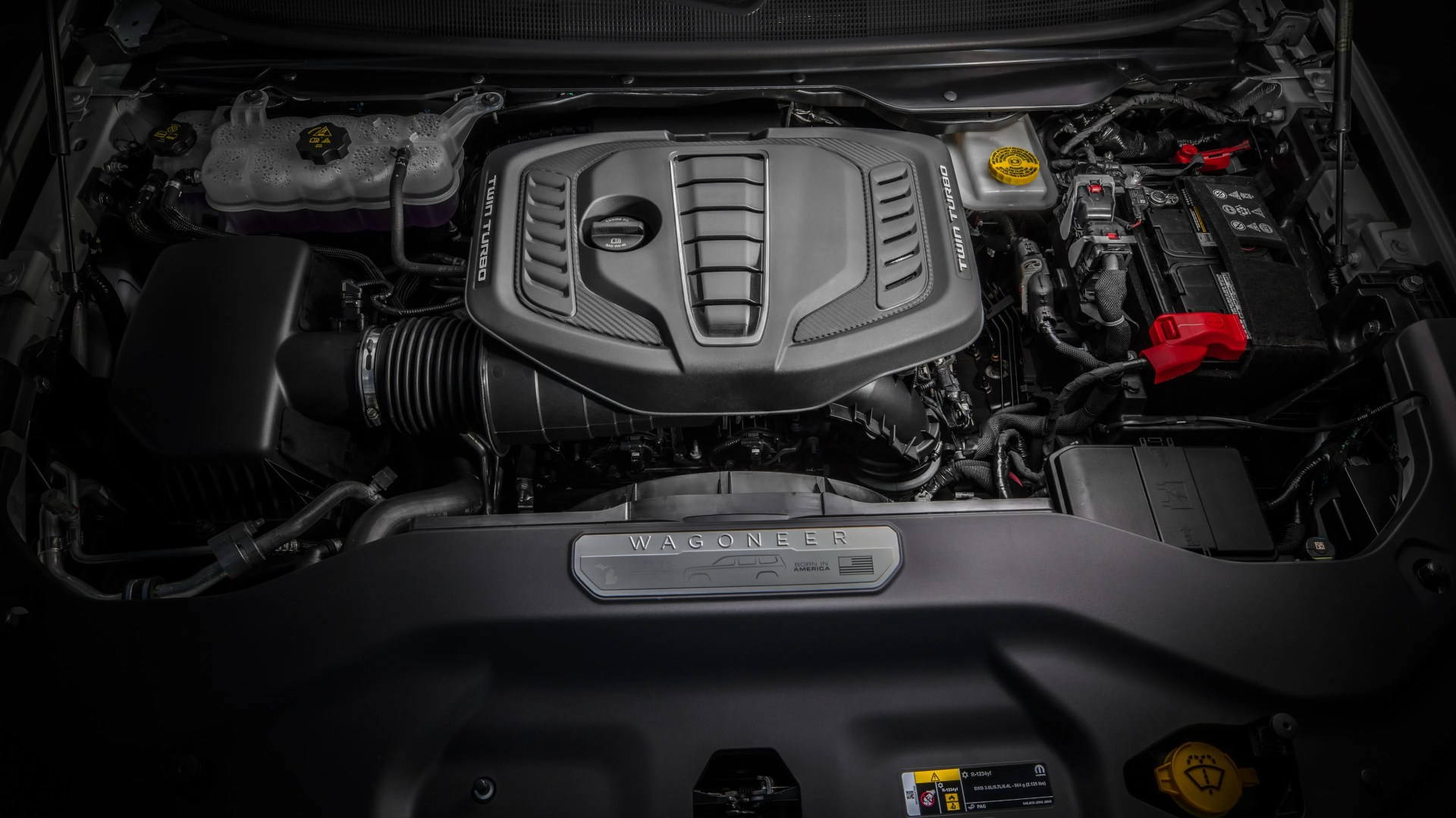 Engine bay of a vehicle with a black engine cover labeled "Twin Turbo" and a "Wagoneer" badge on the front panel.