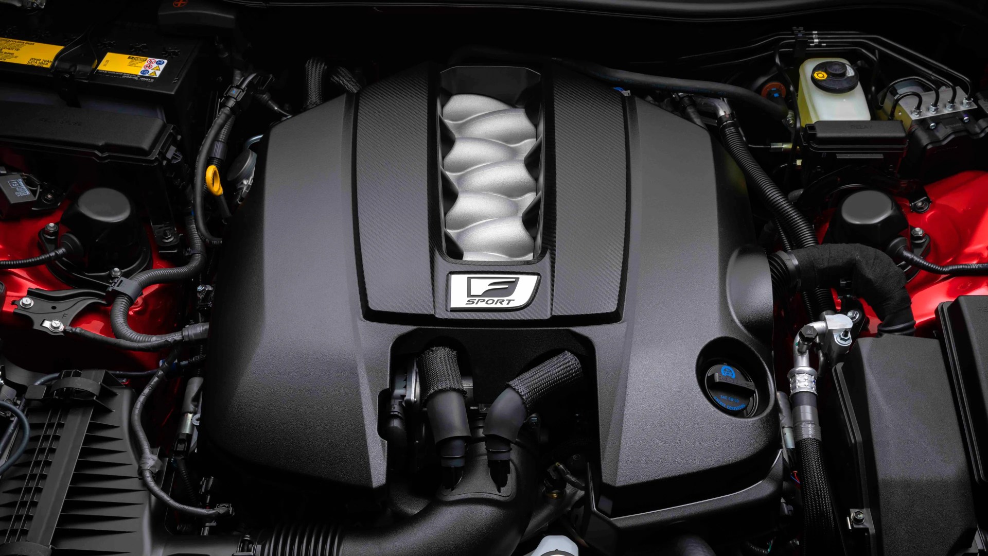 Black engine cover with silver intake manifold and "F Sport" badge in a red engine bay.