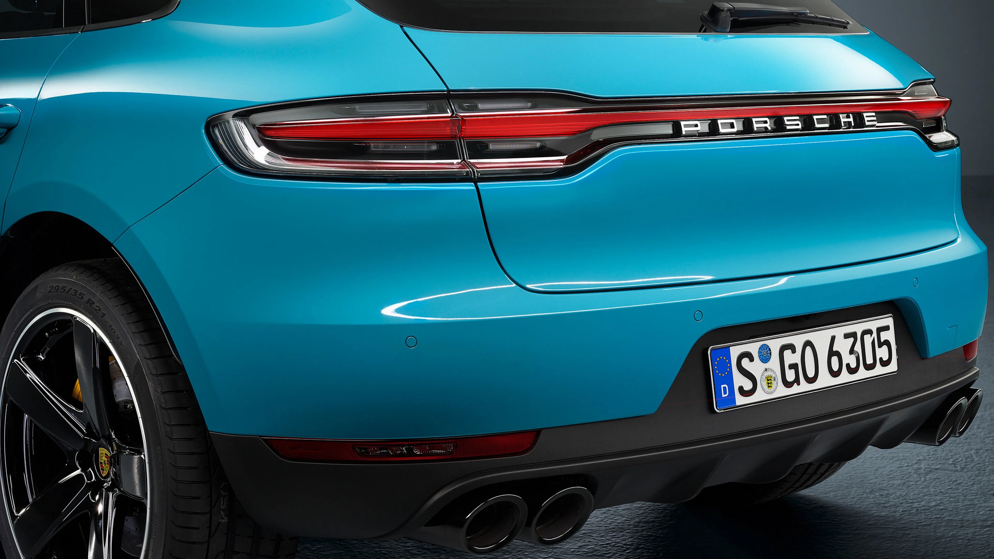 Rear view of a blue Porsche car showing taillights, dual exhaust pipes, and a European license plate.
