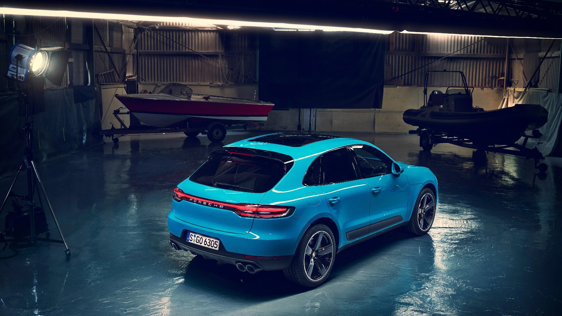 Blue Porsche Macan SUV with black roof and quad exhausts in a dimly lit garage with boats.