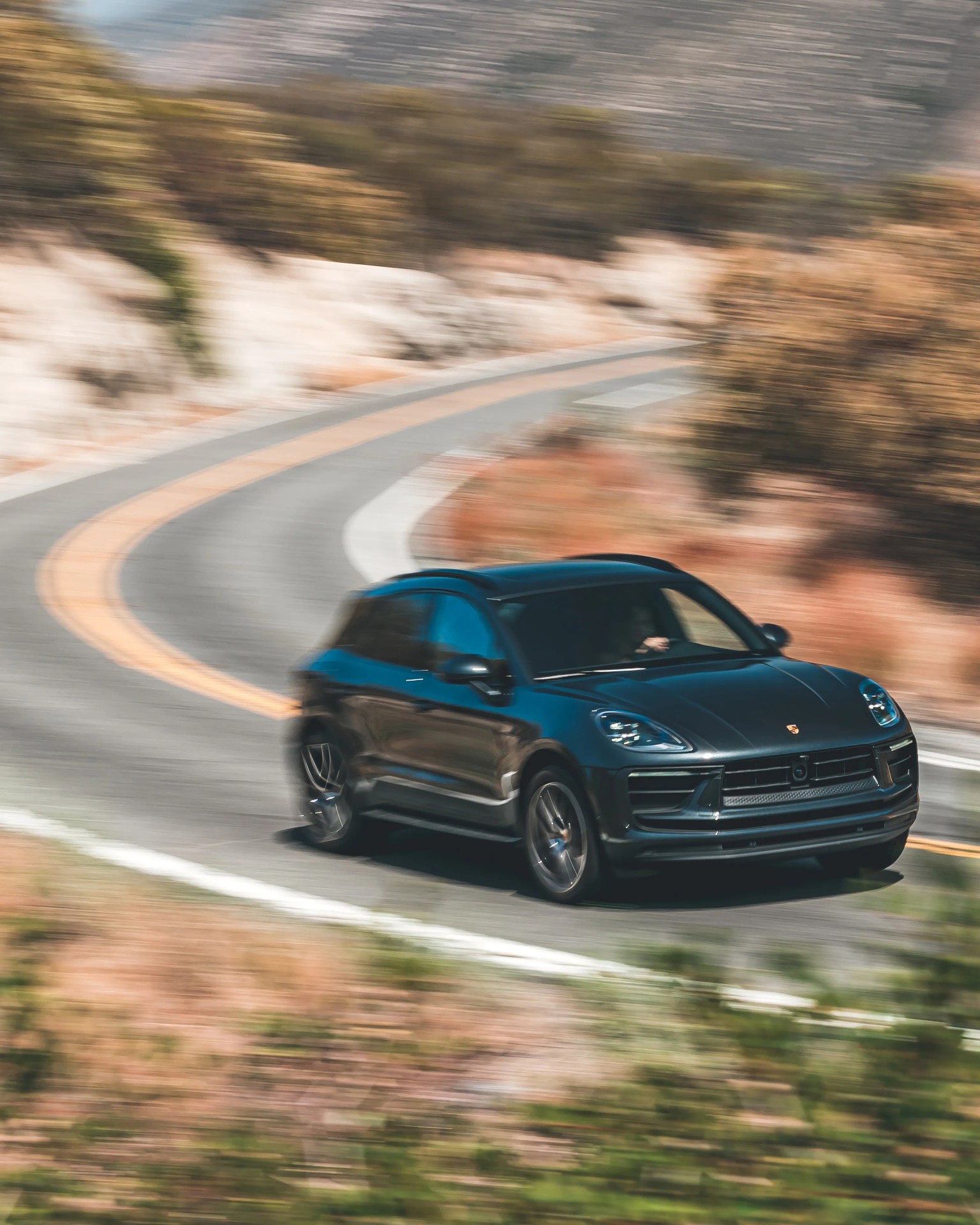 Black Porsche SUV driving fast on a winding mountain road with blurred background.