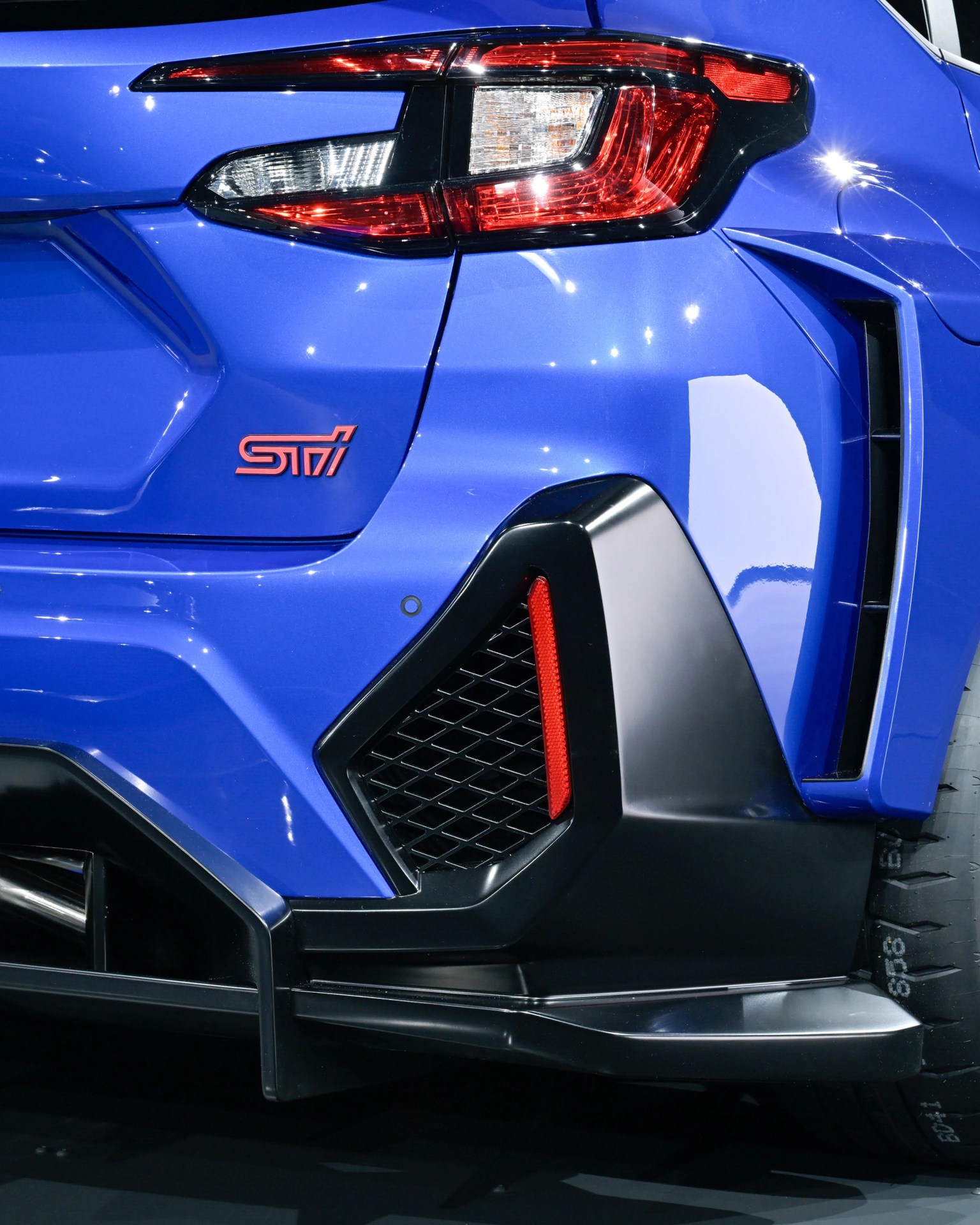 Close-up of the rear right side of a blue Subaru STI with red and white taillights and black aerodynamic trim.