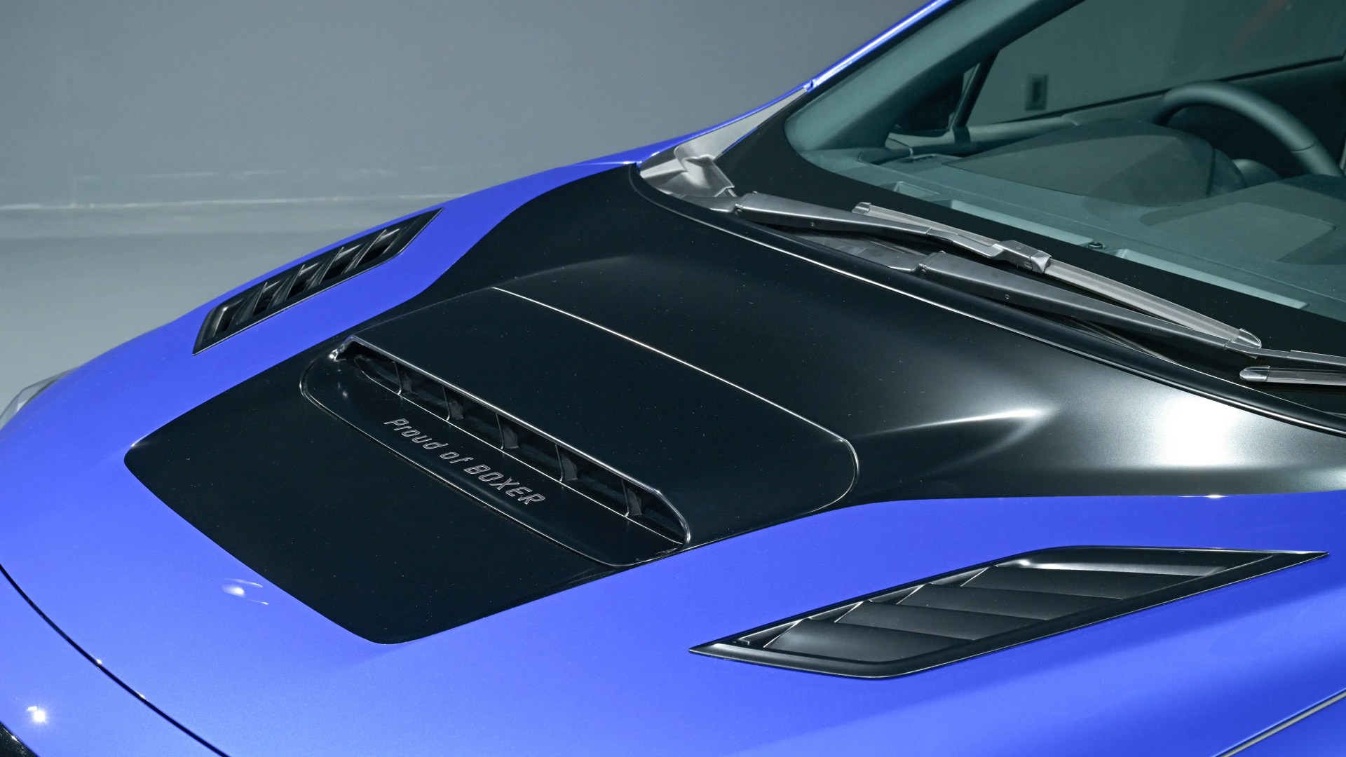 Blue car hood with black vents and "Proud of BOXER" text near the windshield wipers.