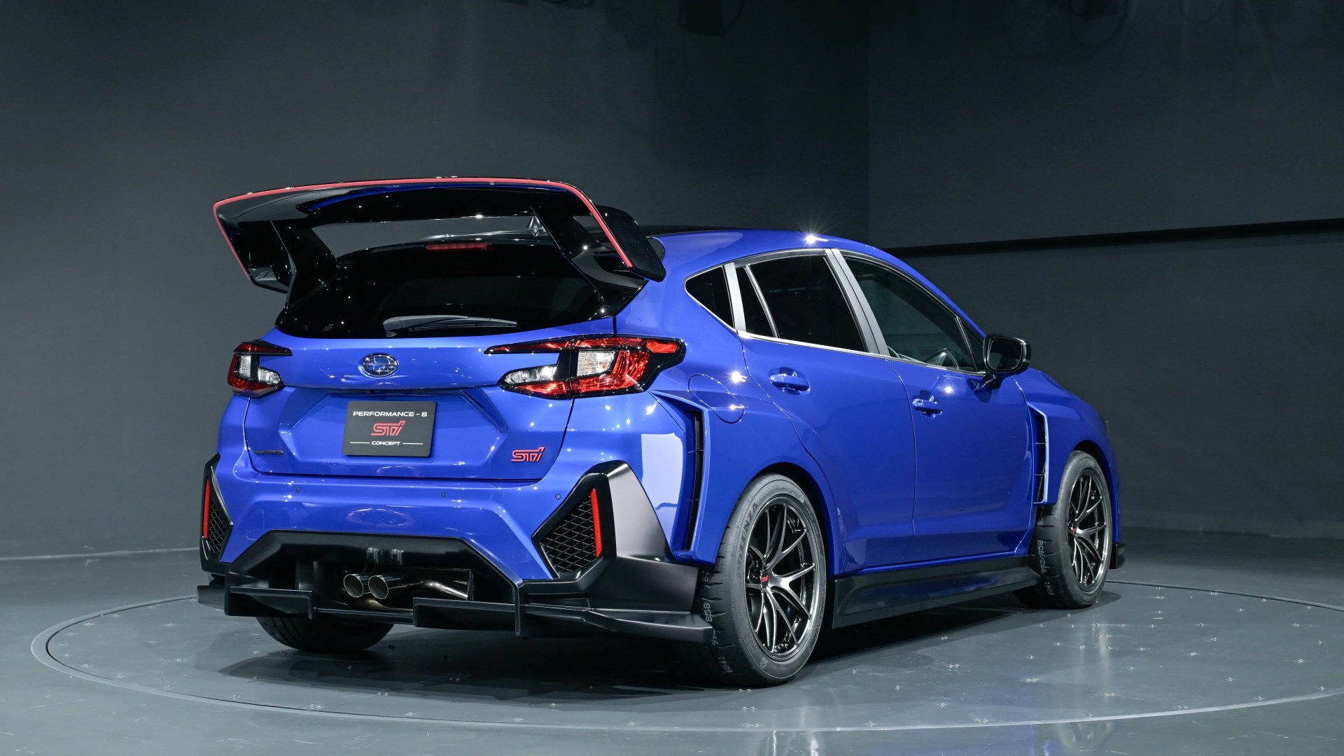 Blue Subaru hatchback with large rear spoiler and black alloy wheels in a studio.